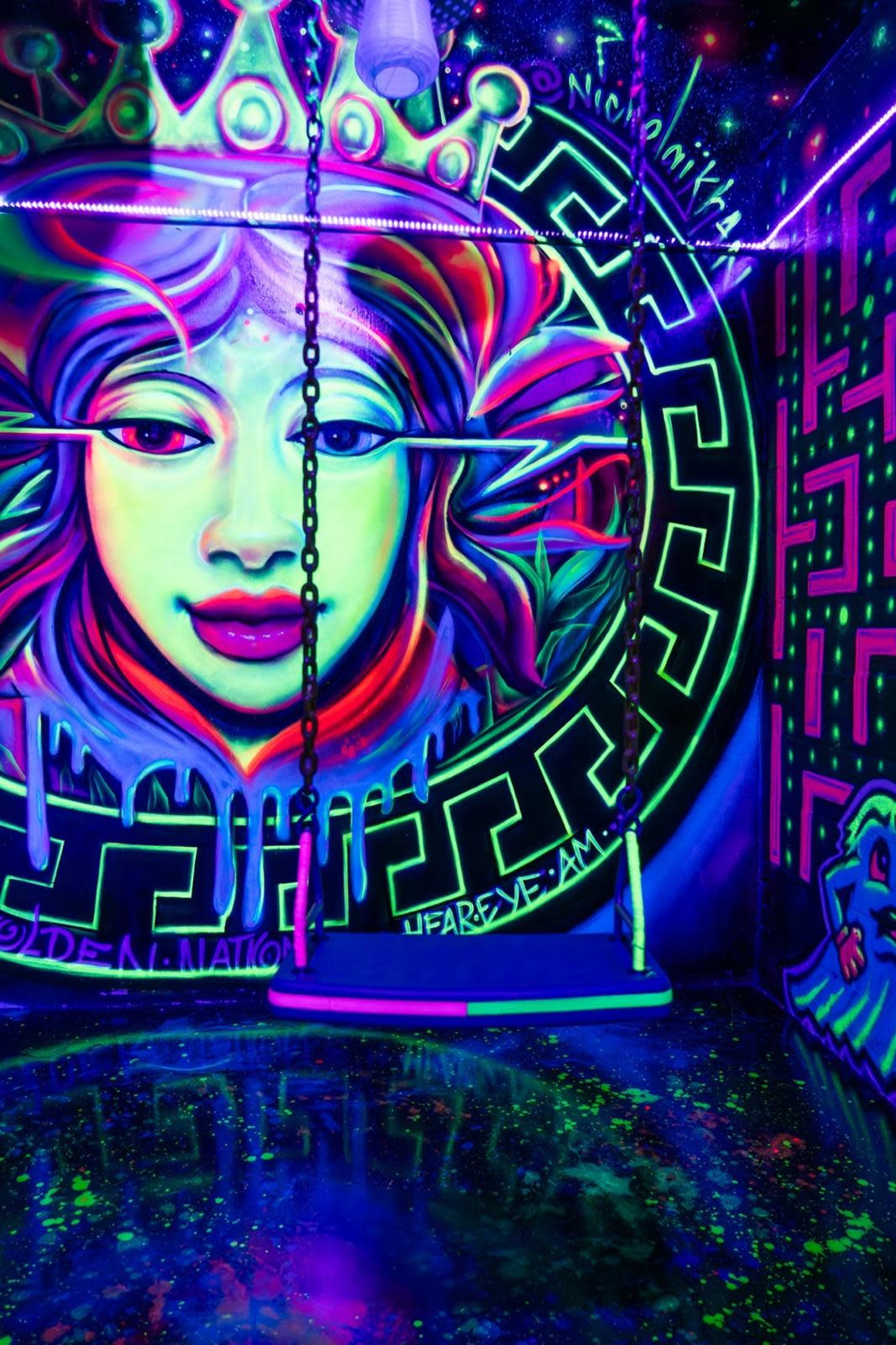 A brightly colored mural featuring a woman's face with vibrant patterns and a swing set against a neon-lit wall.
