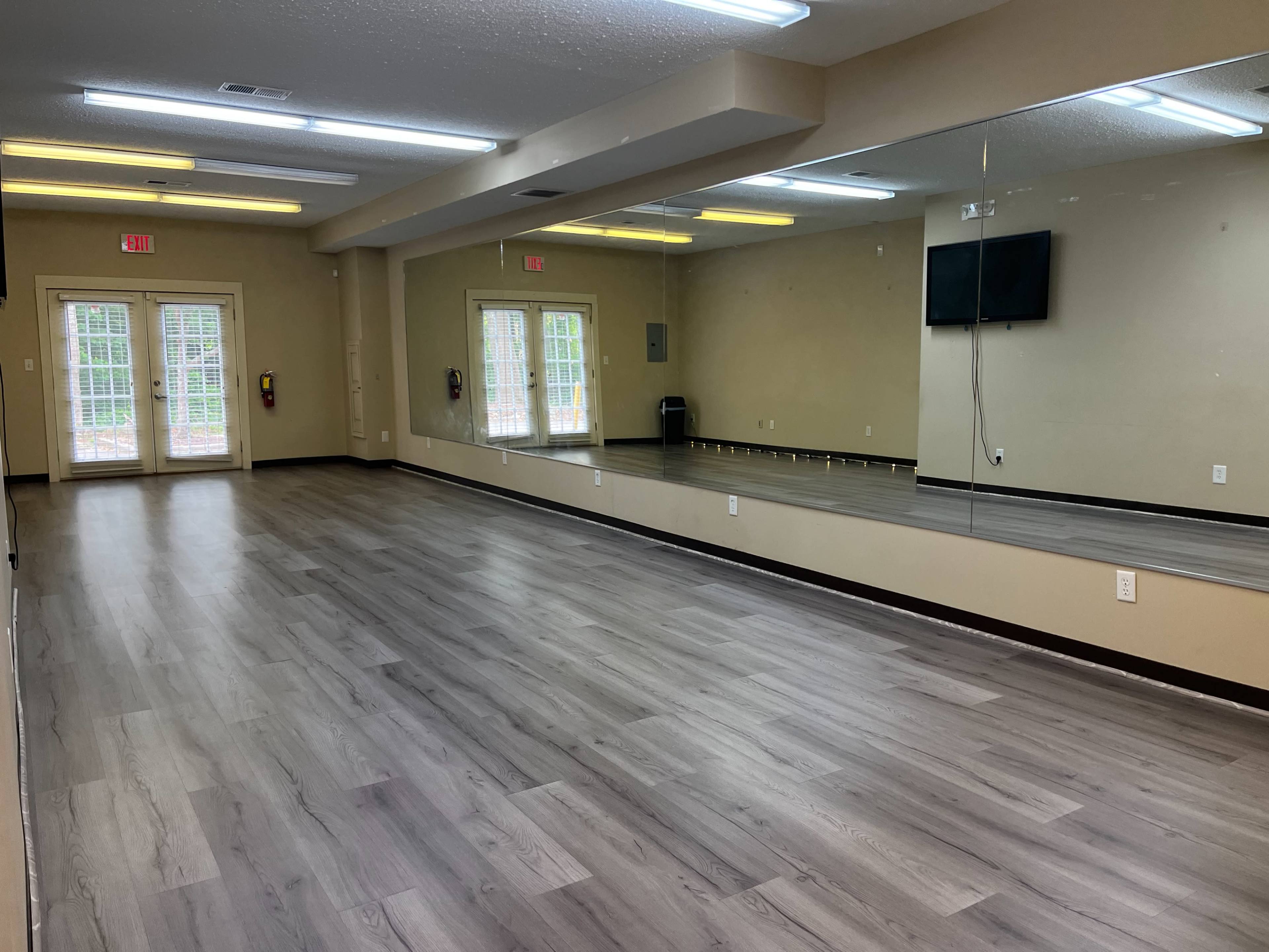 A spacious room with wooden flooring, large mirrors on one wall, and two sets of double doors leading outside.