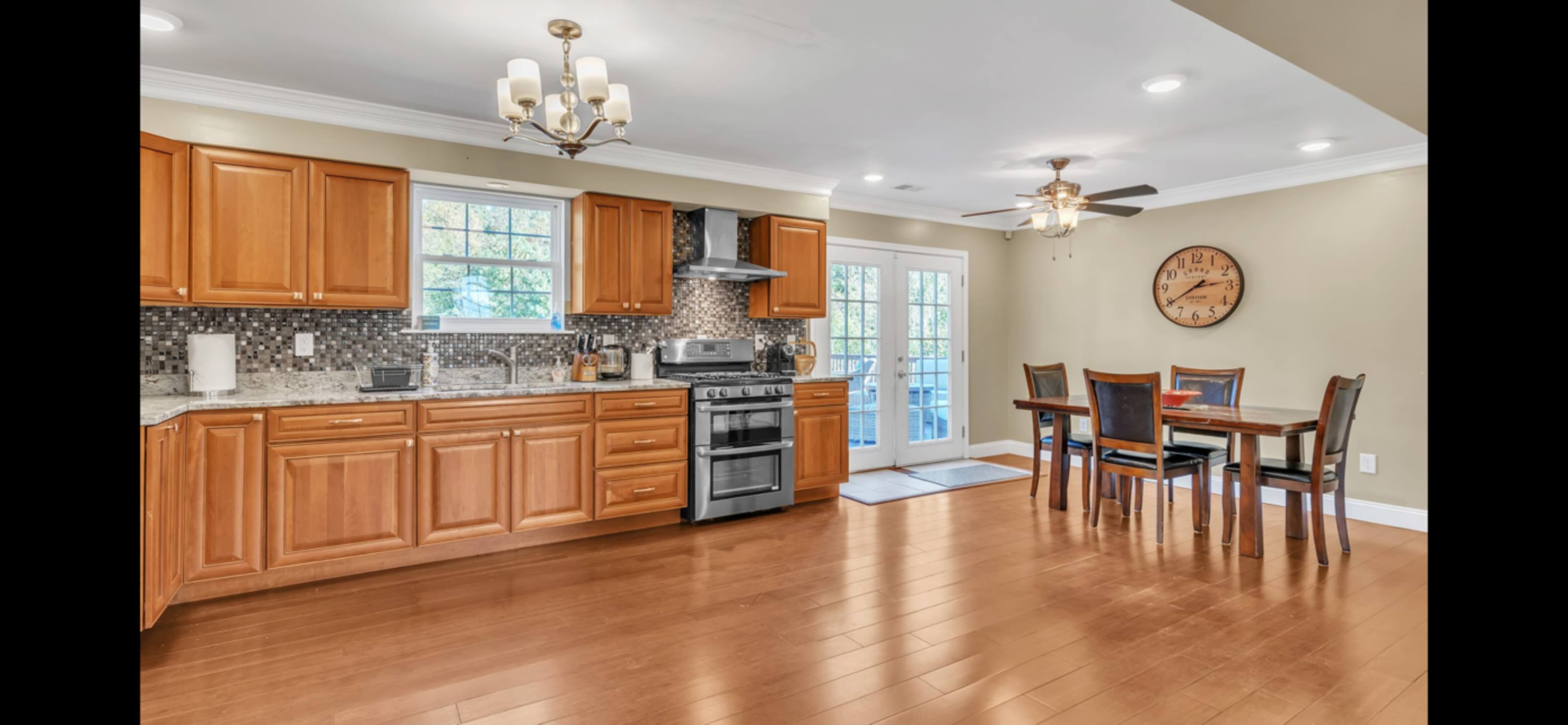 A modern kitchen with wooden cabinetry, stainless steel appliances, and a dining area featuring a table and chairs near a set of French doors.