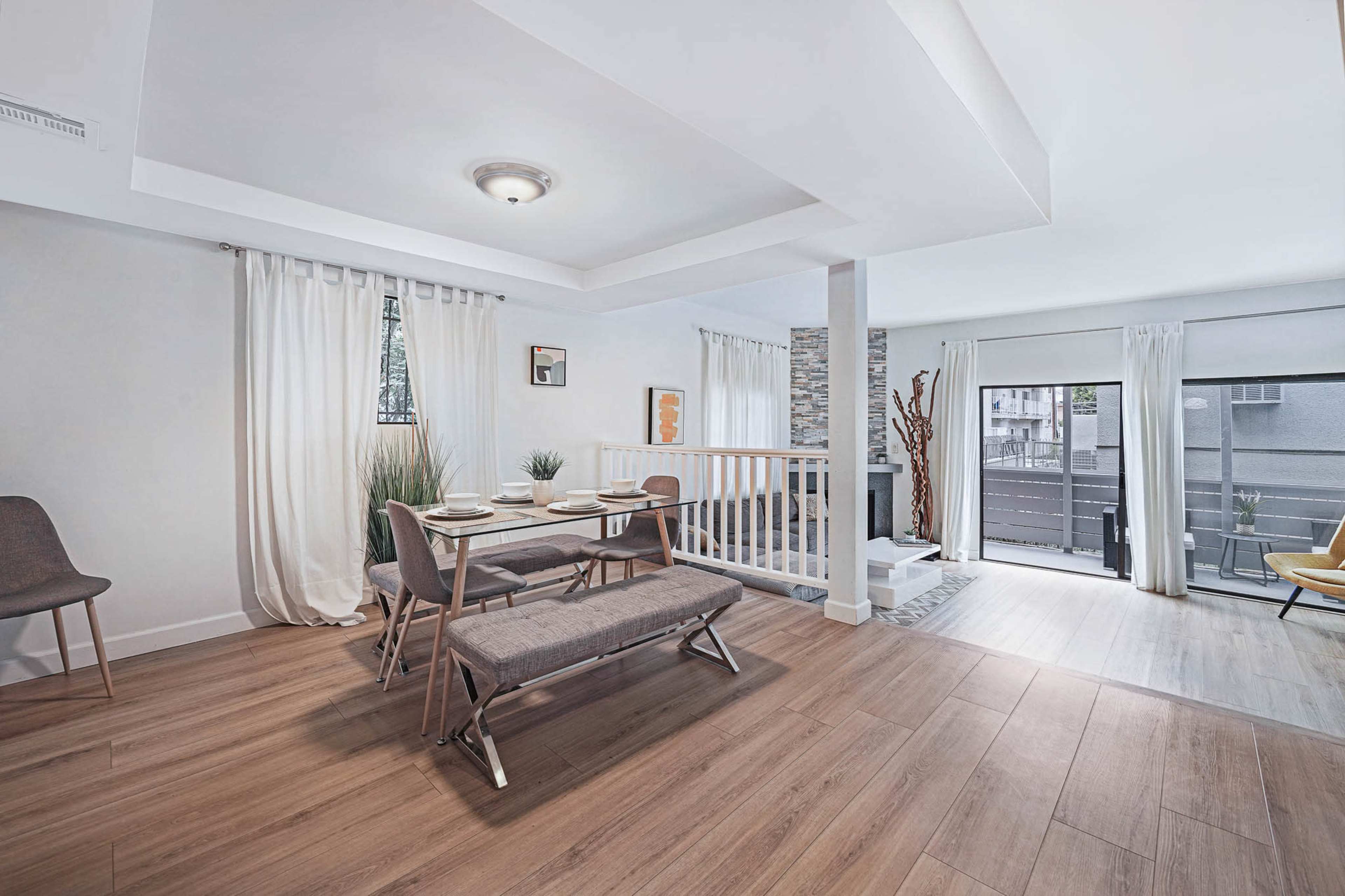 The image shows a modern dining area with a bench and table setup, hardwood floors, and large windows allowing natural light.