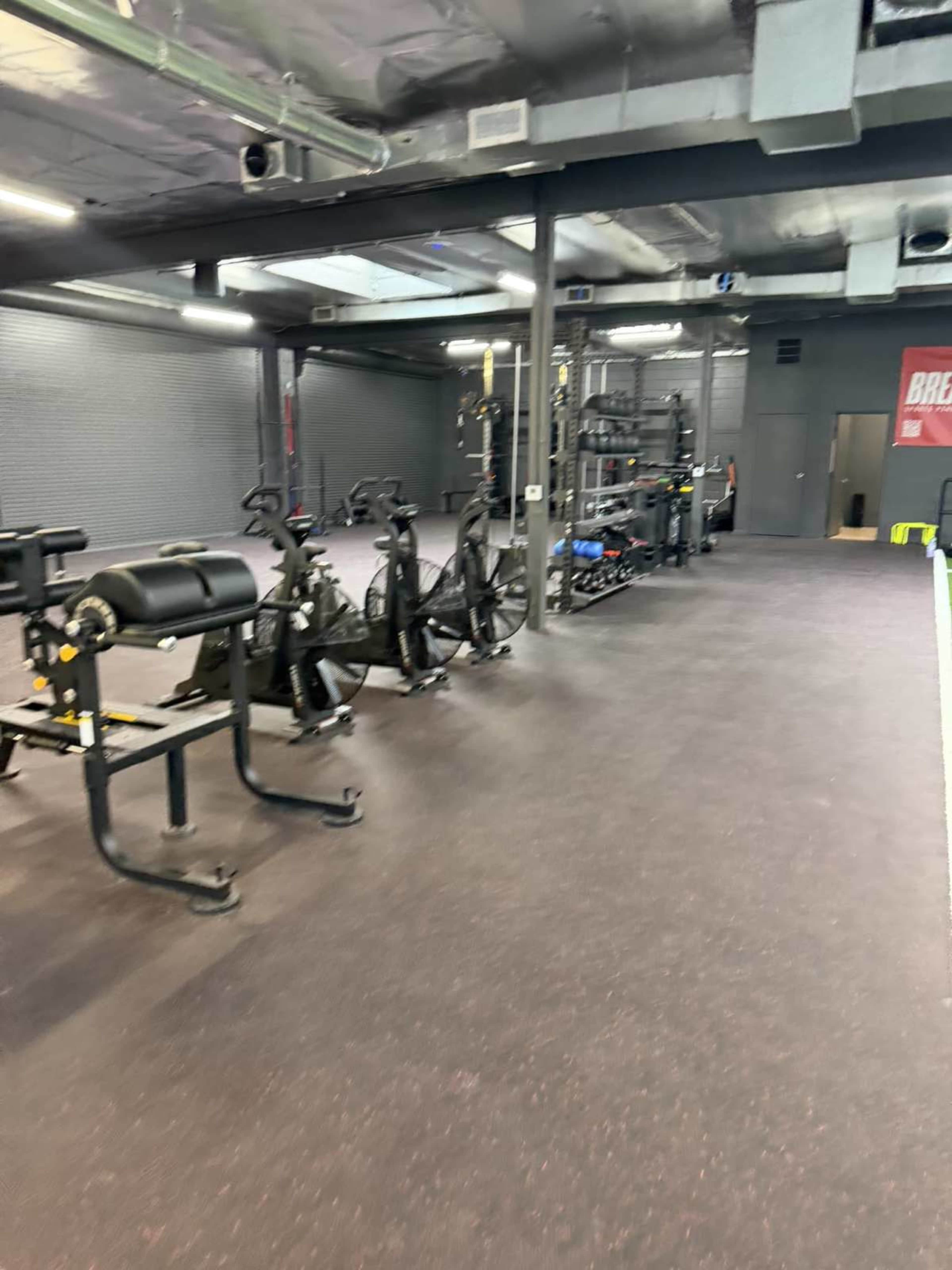 The image shows an empty gym space equipped with exercise machines and strength training equipment arranged along the walls.