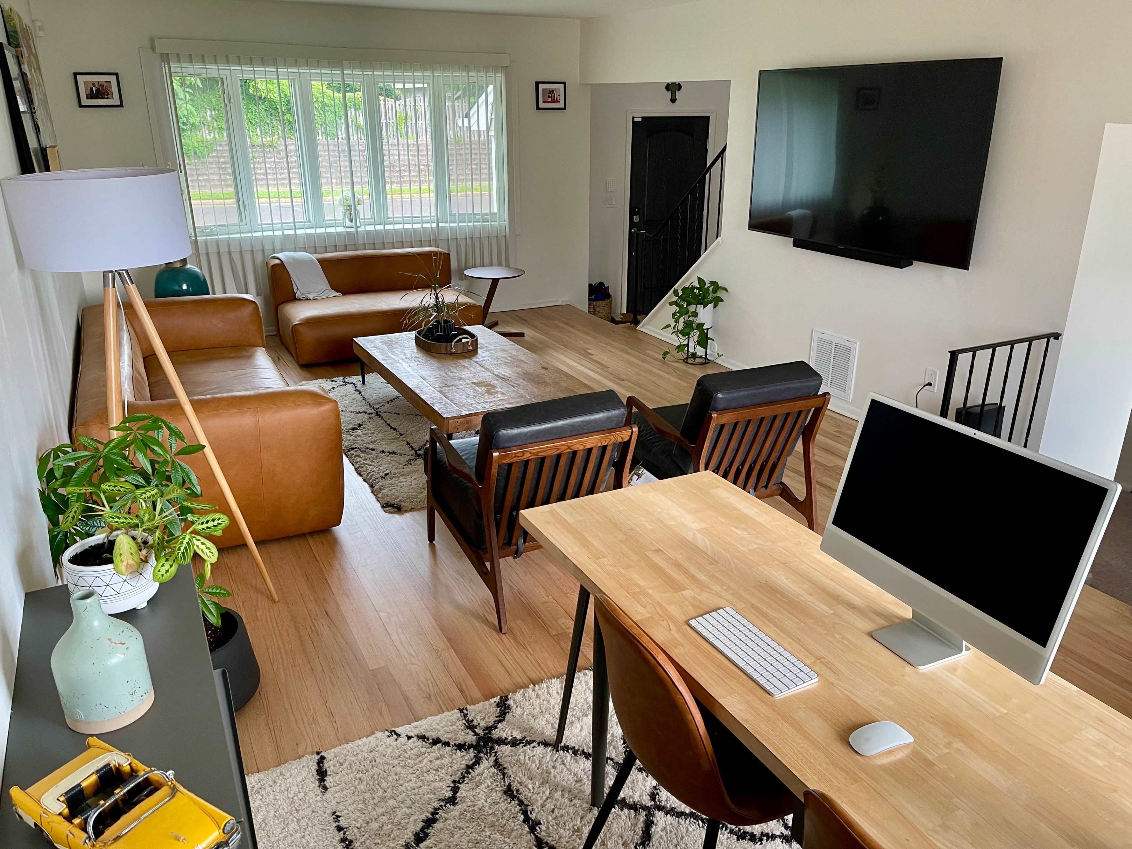 A modern living room with brown leather furniture, a wooden coffee table, a TV mounted on the wall, and a workspace featuring a computer desk.