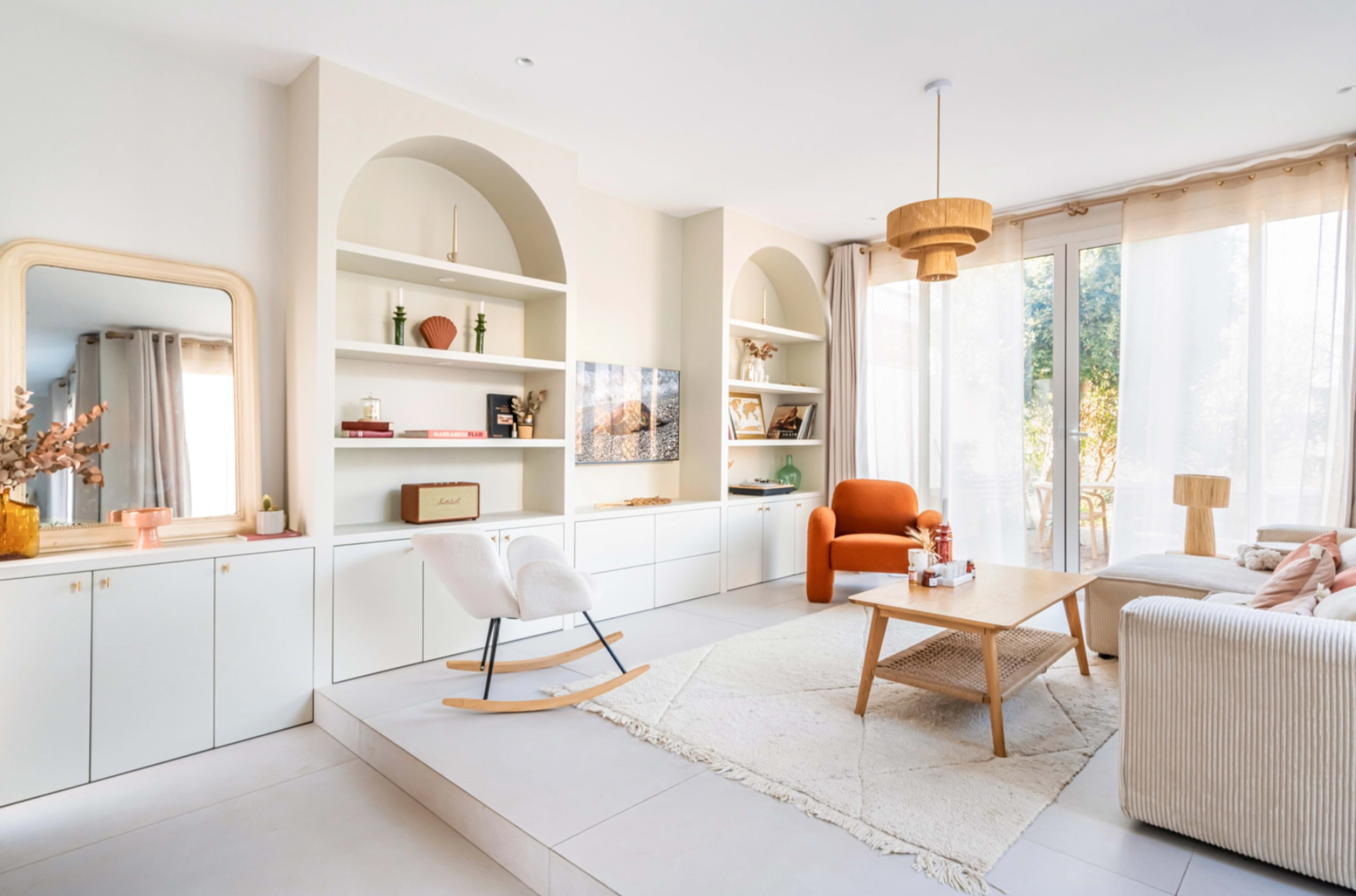 A modern living room with built-in shelves, a rocking chair, and large windows allowing natural light to enter the space.