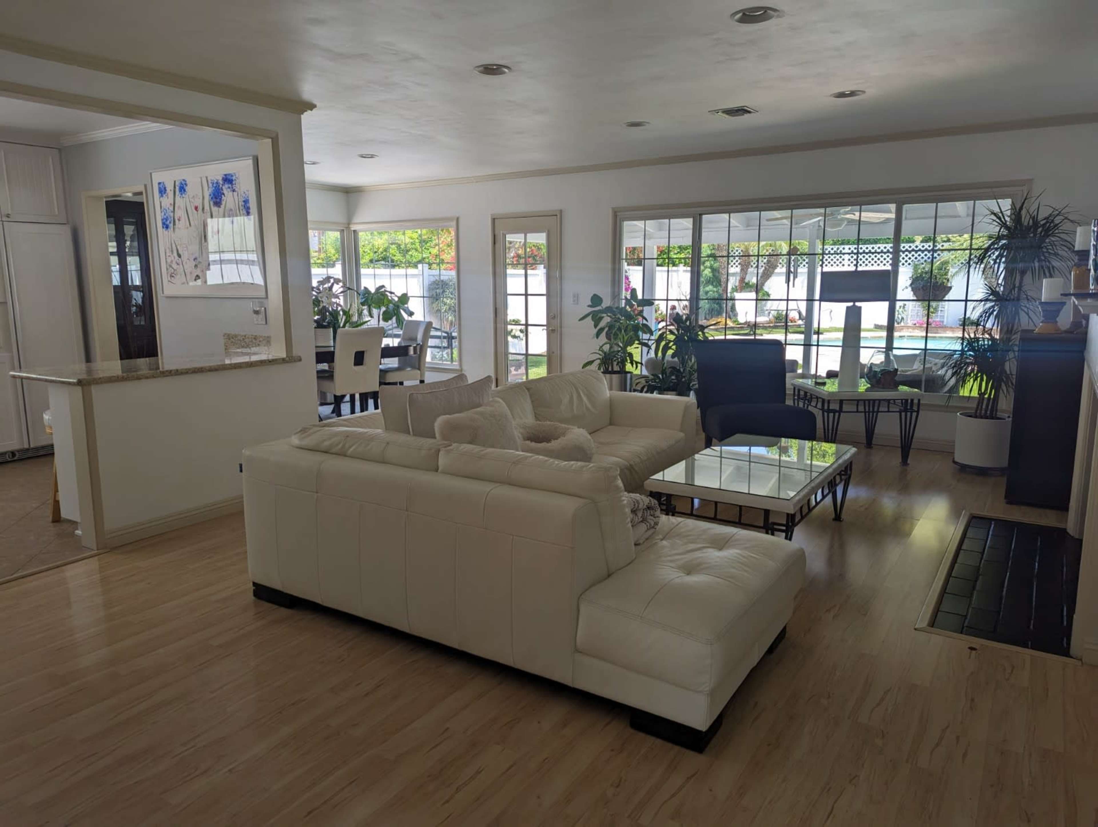A spacious living area with a white sectional sofa, a glass coffee table, and large windows allowing natural light to illuminate the room.