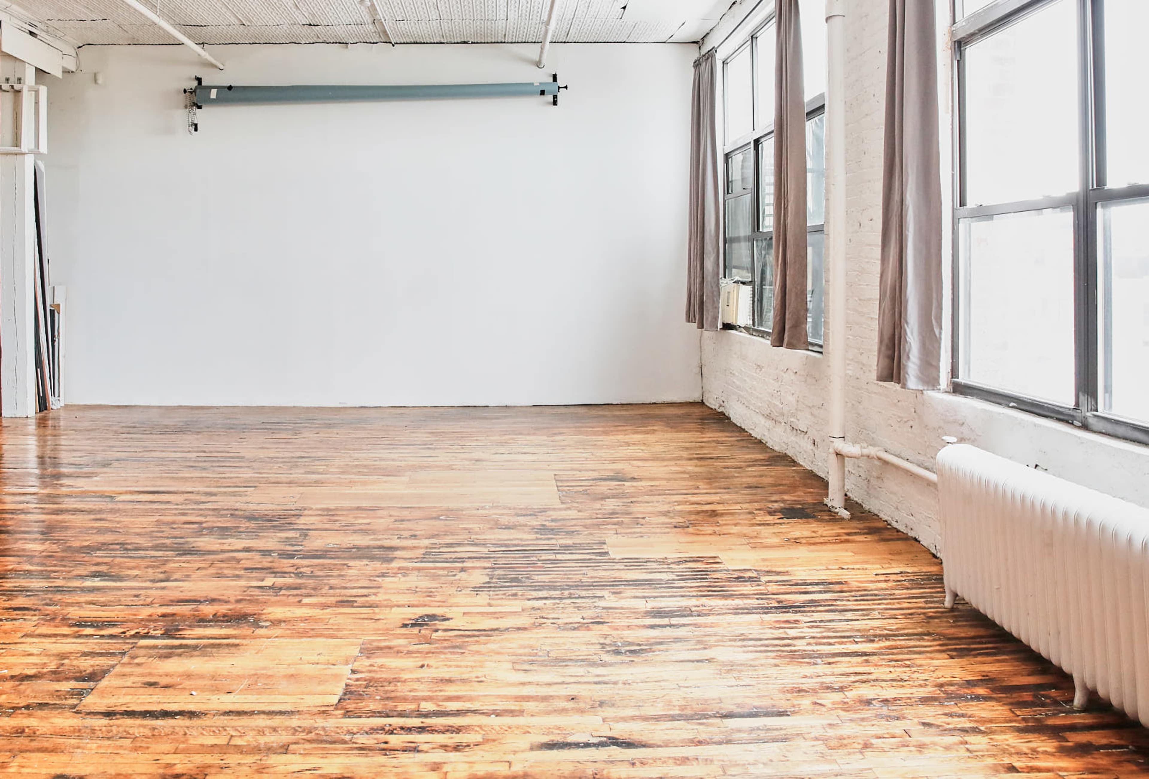 A spacious, empty room with large windows, wooden flooring, and white walls.