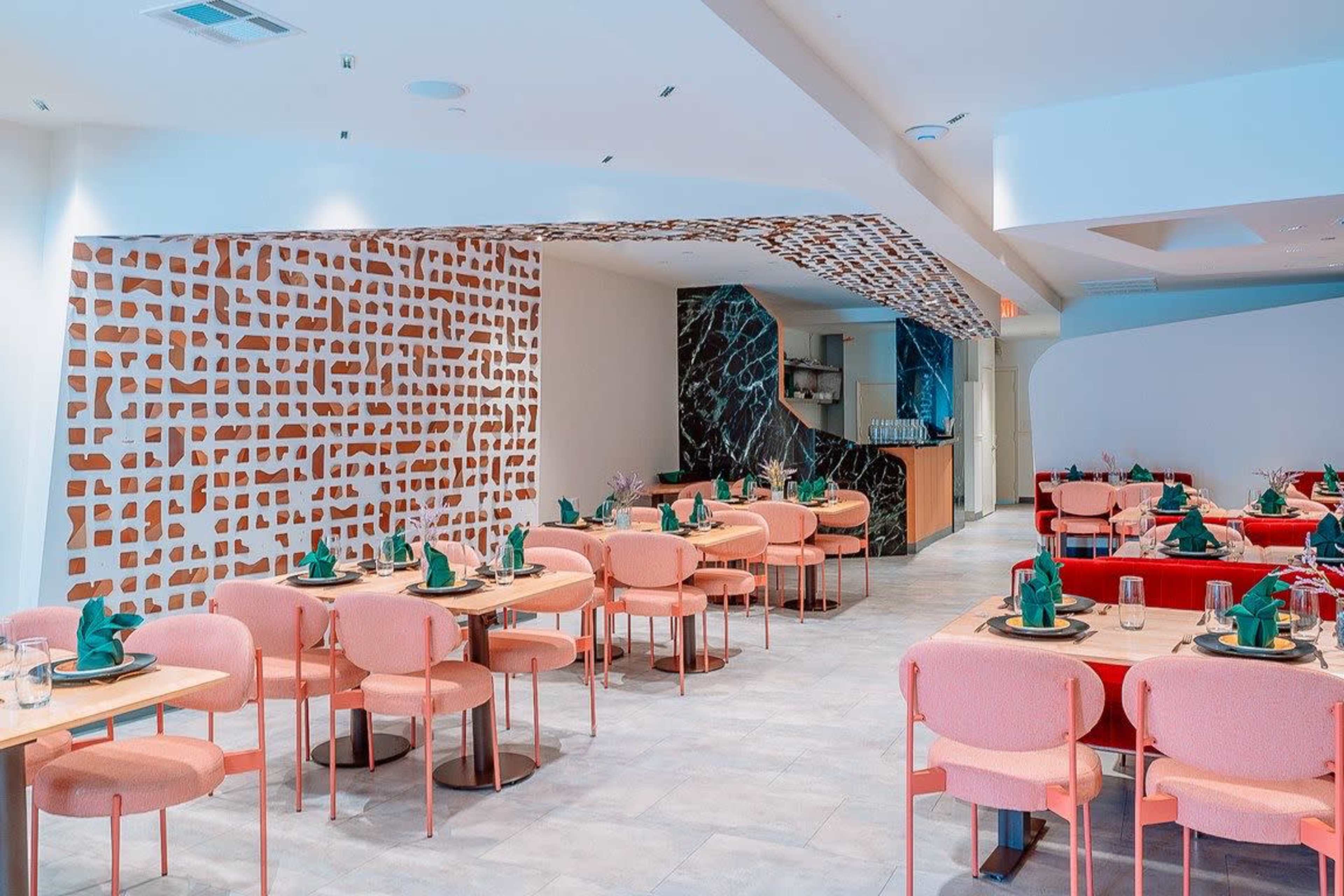 The image shows a modern restaurant interior with pink chairs, green table settings, and decorative walls featuring abstract patterns.