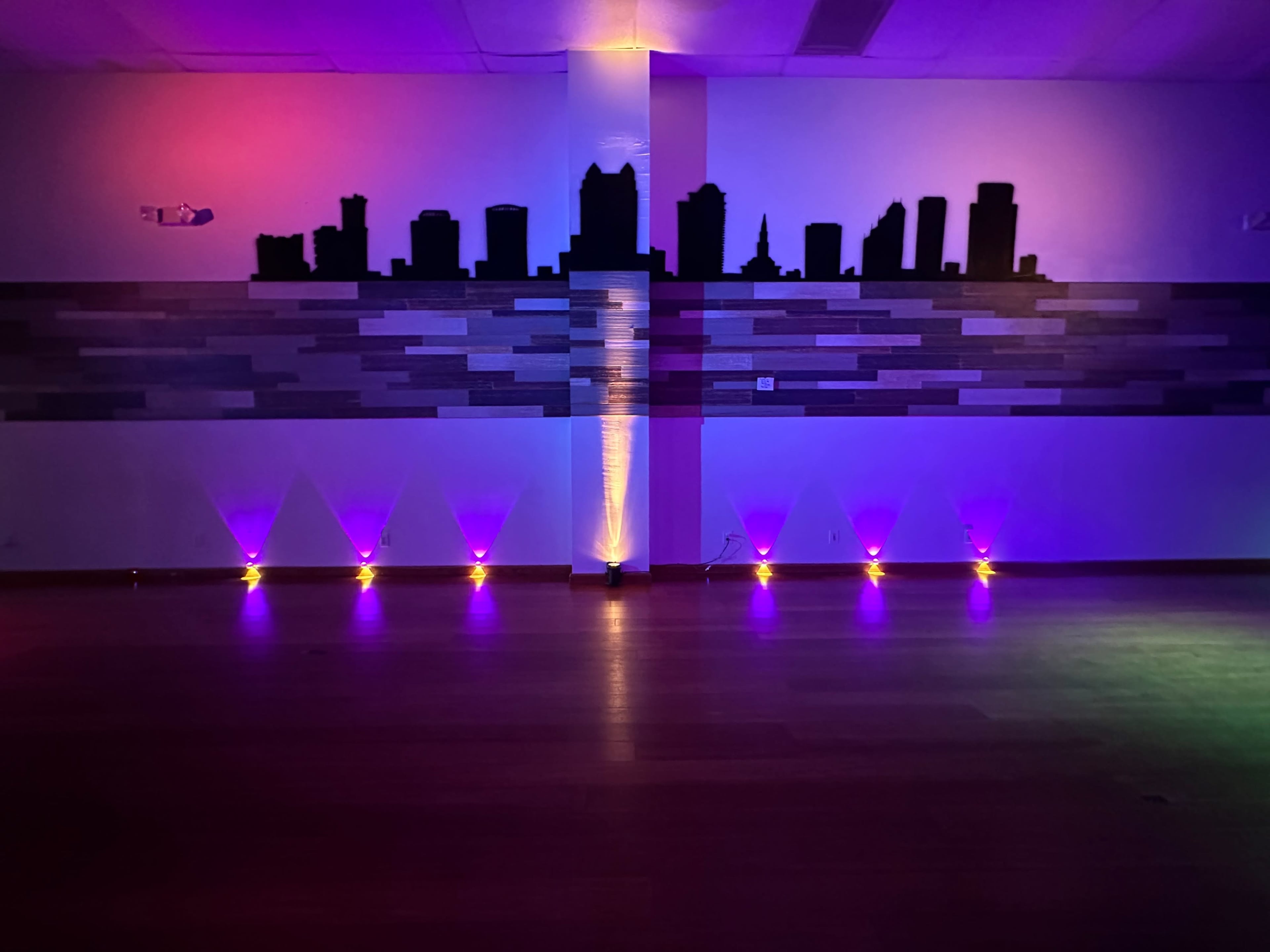 A dark room with a silhouetted city skyline on the wall, illuminated by colorful lights at the bottom.