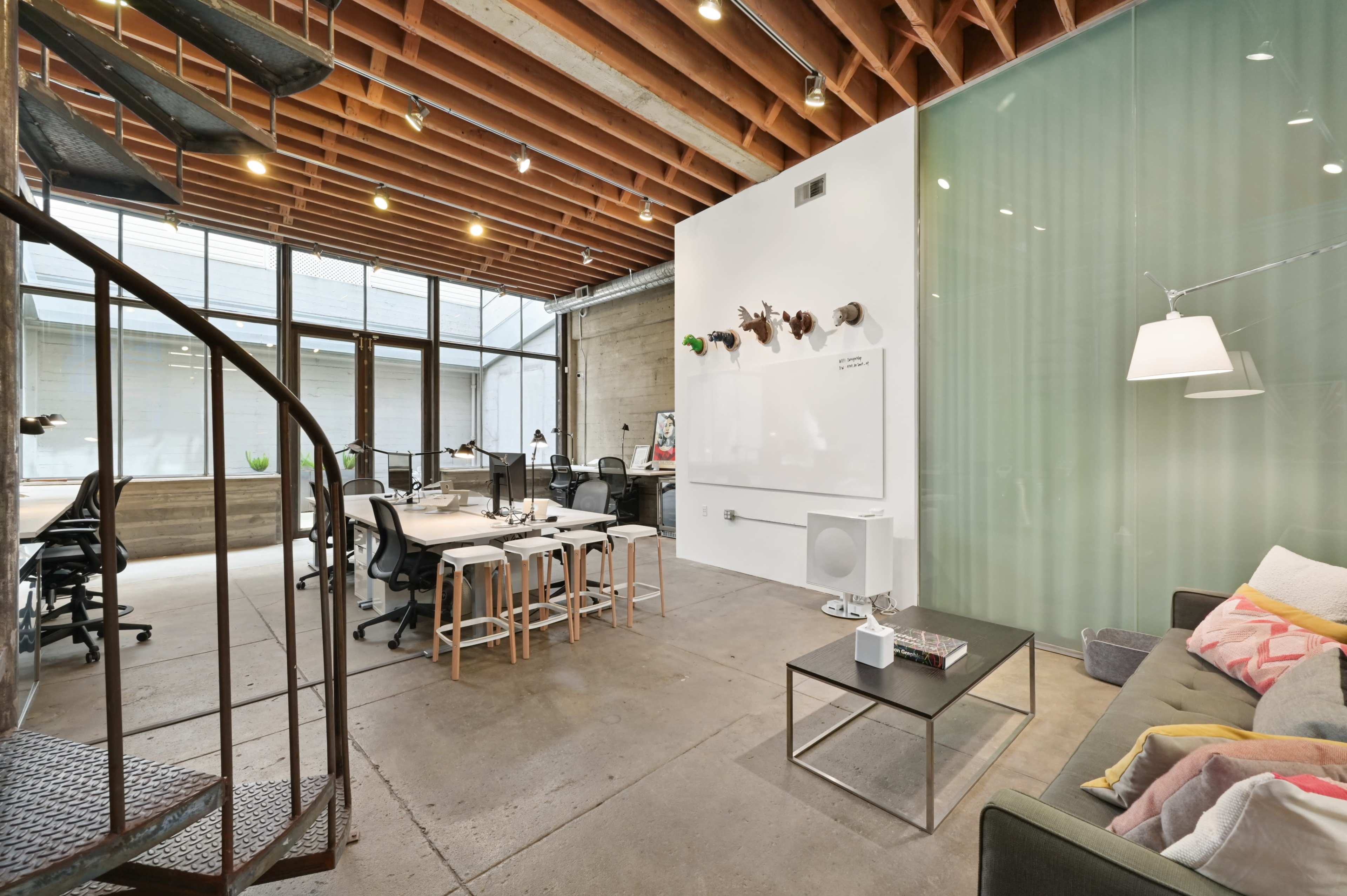 A modern, open office space with a mix of desks, a lounge area, and exposed wooden beams overhead.