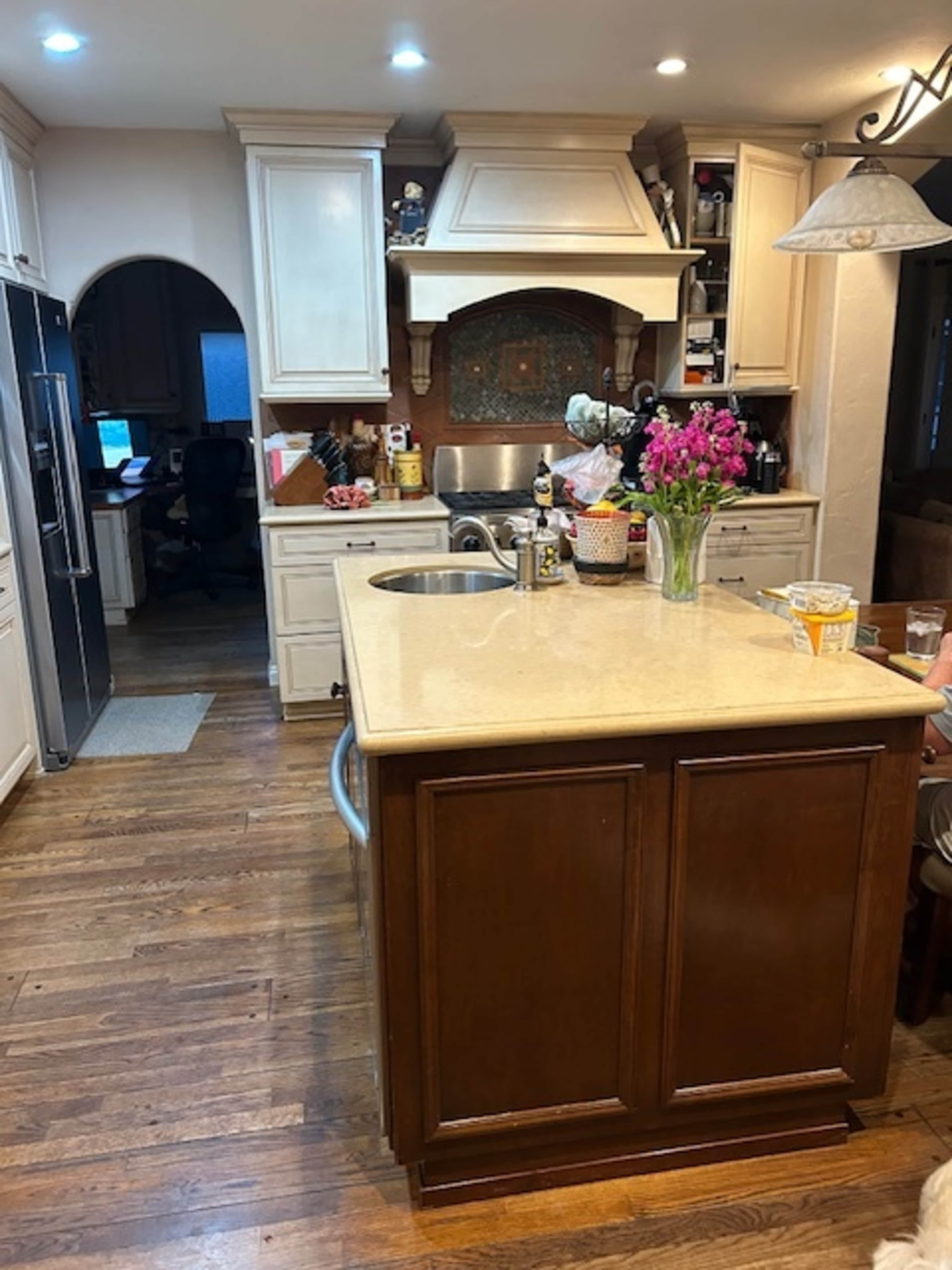 A kitchen with light-colored cabinetry, a central island, a stainless steel sink, and a bouquet of flowers on the countertop.