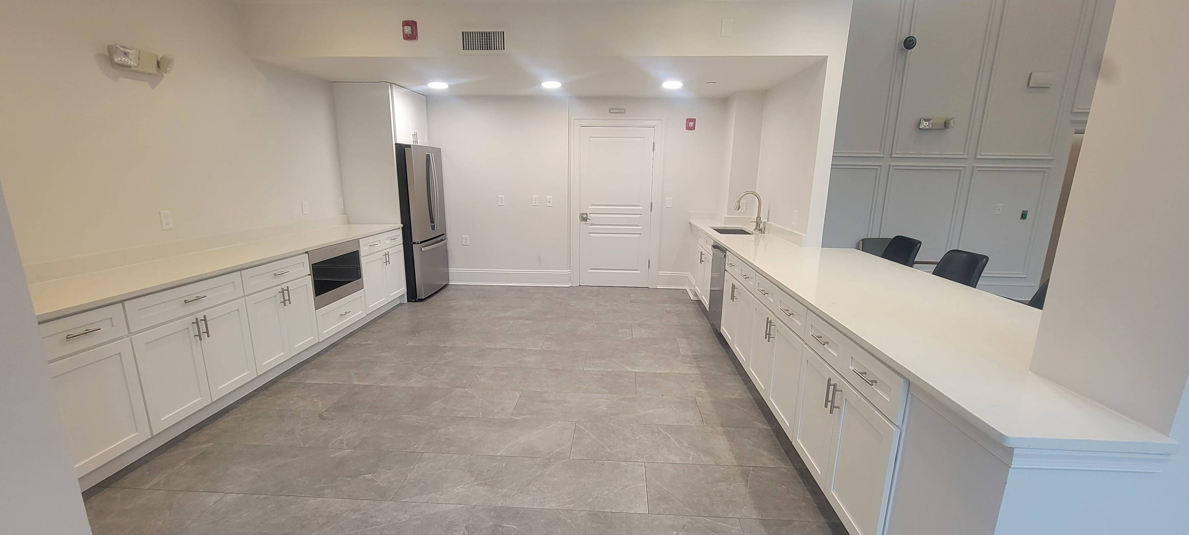 The image shows a modern kitchen with white cabinetry, stainless steel appliances, and gray tile flooring.