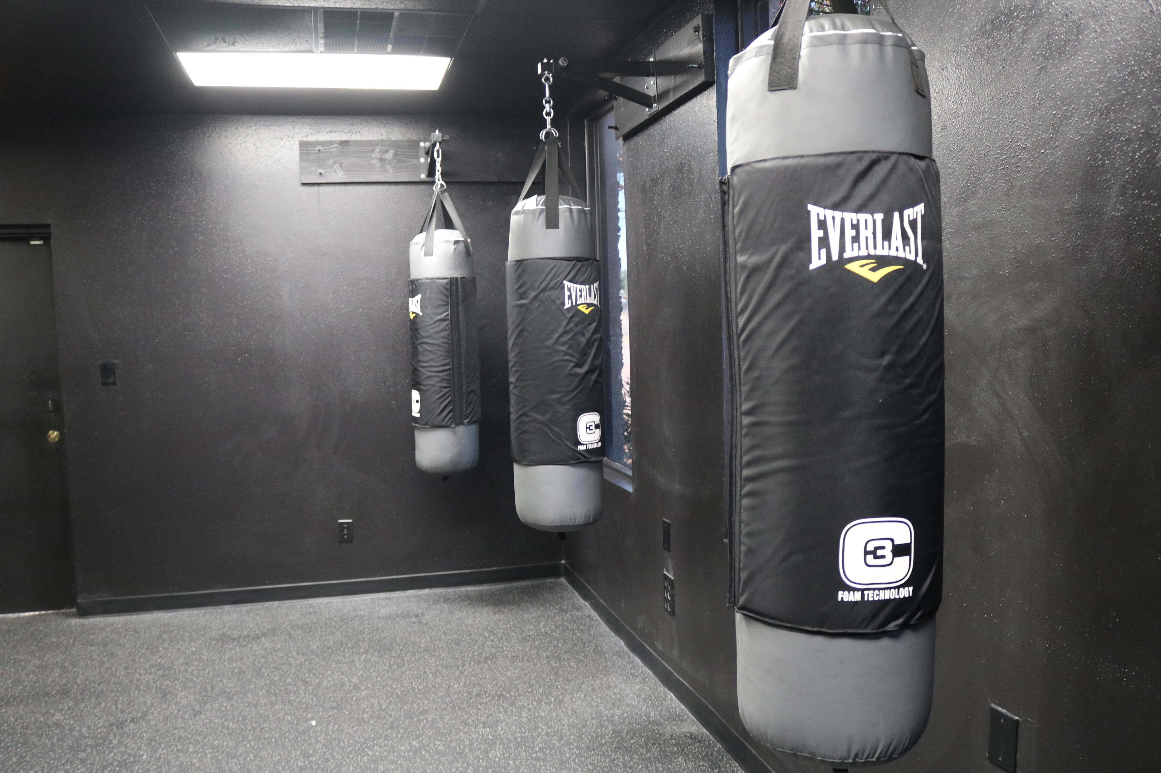 Three black Everlast punching bags hang from the ceiling in a dimly lit gym.