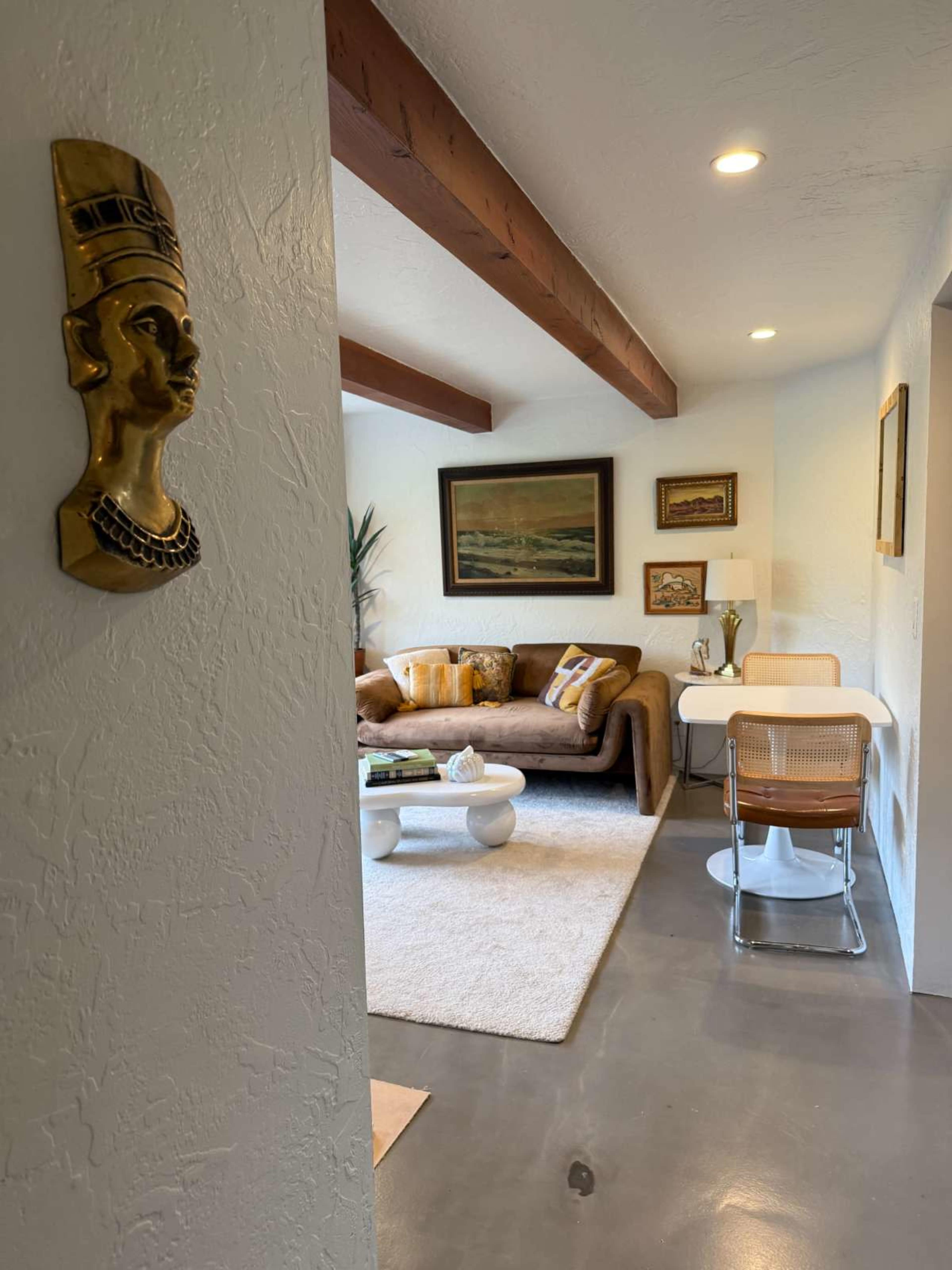 A narrow hallway leads into a cozy living area with a brown couch, a coffee table, and artworks on the walls.