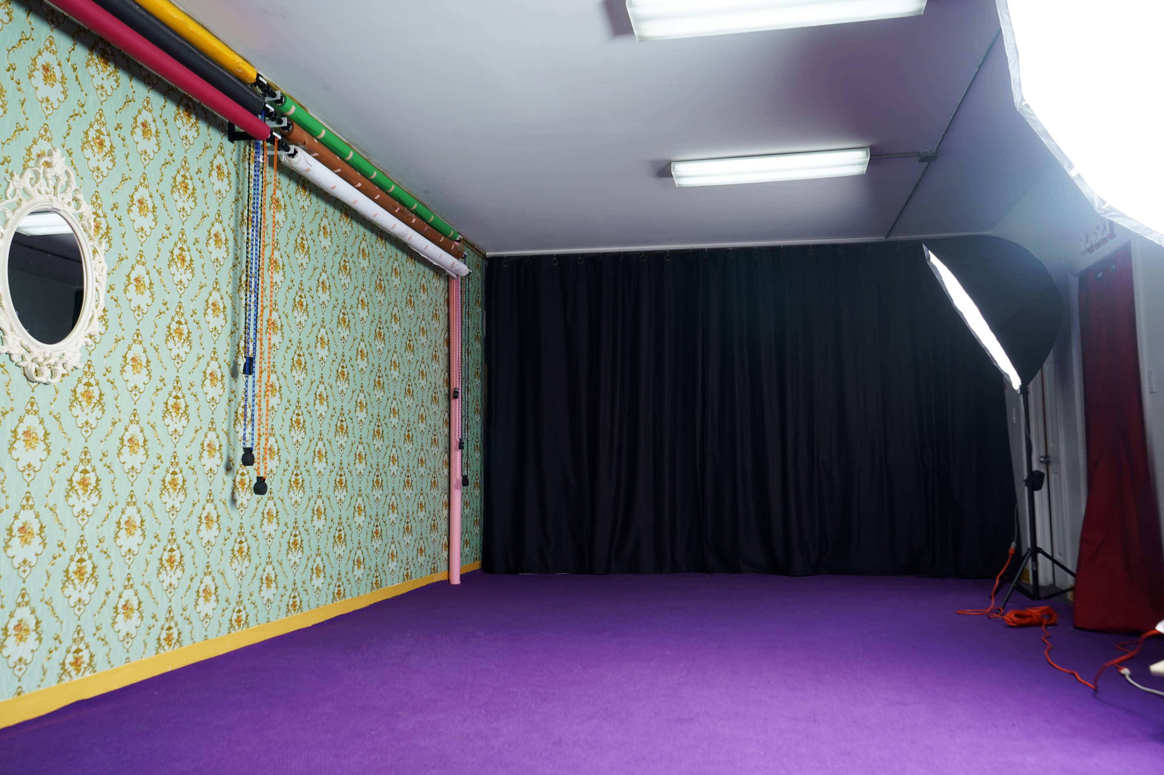 A photography studio with a patterned green wall, purple carpet, and a mix of lighting equipment set up in a corner.