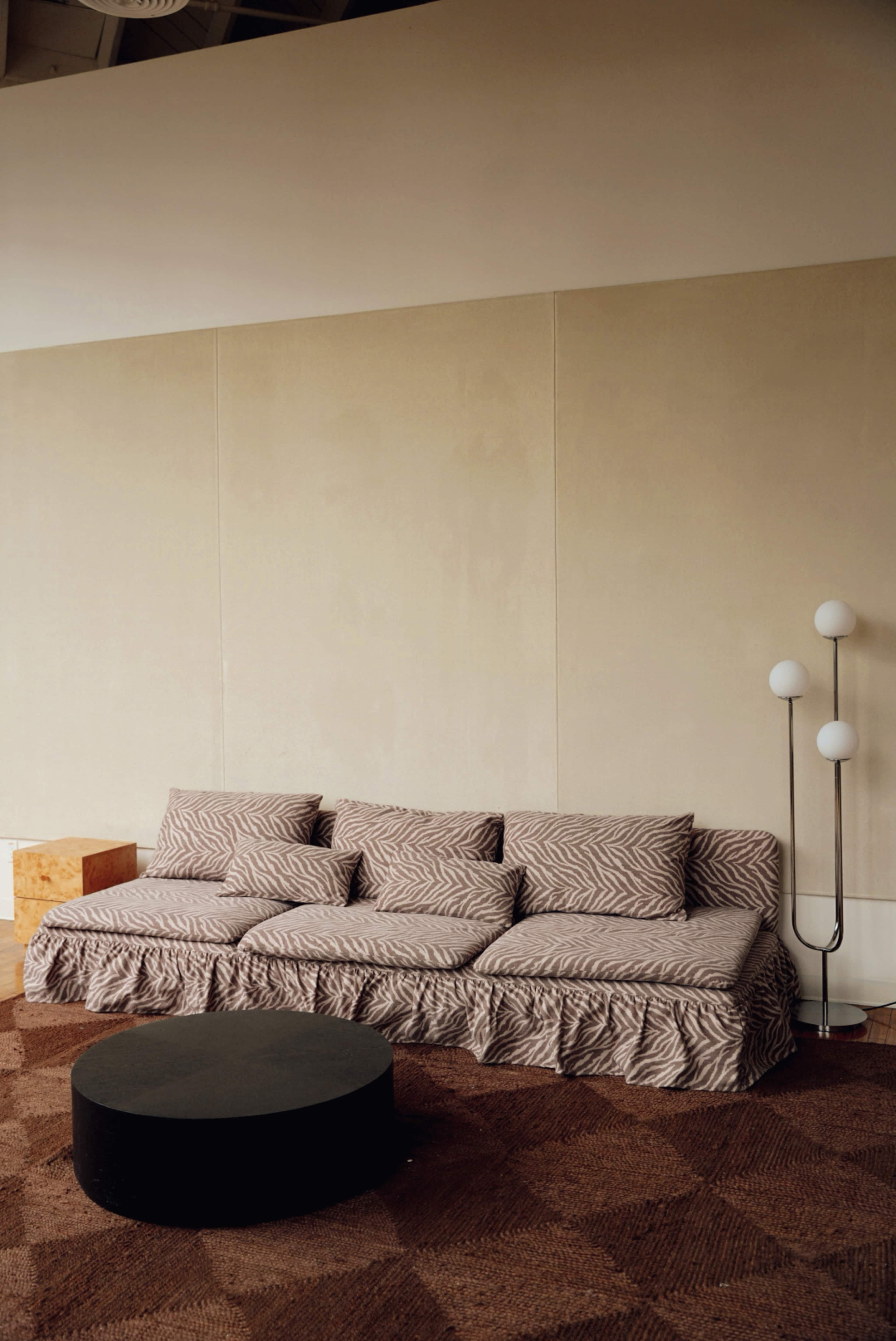 The image shows a modern interior space featuring a patterned sofa, a round black coffee table, and a floor lamp with three white globes.