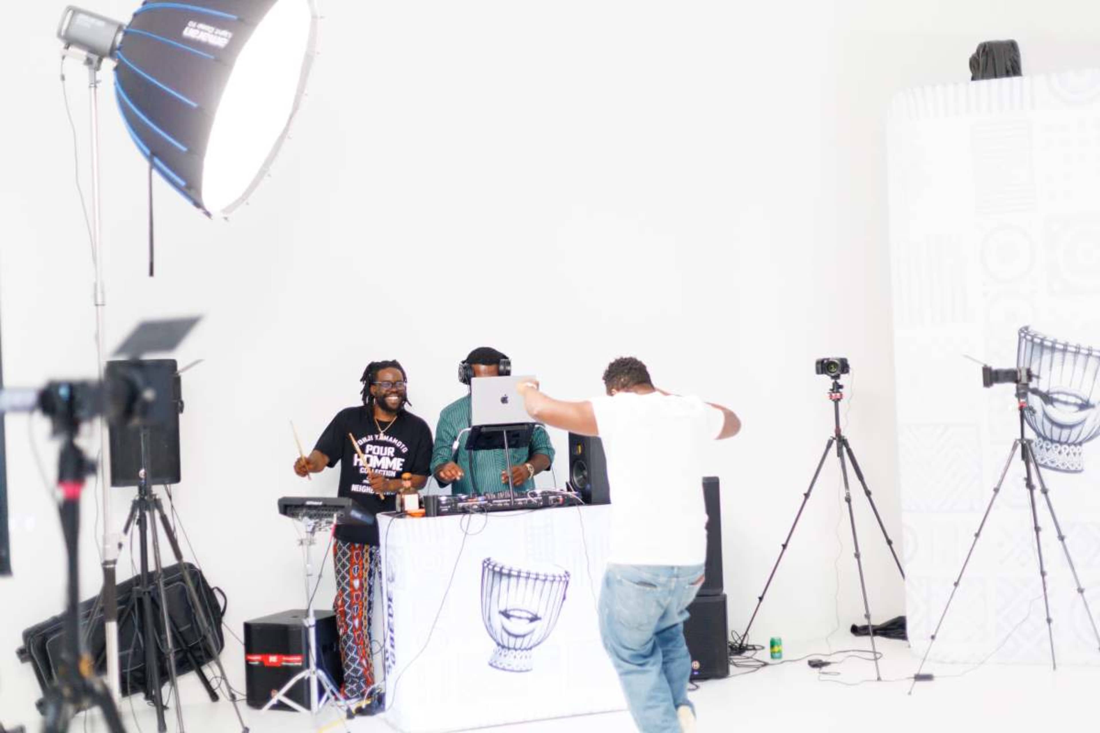 A DJ performs at a studio with two musicians, while a dancer moves in front of them.