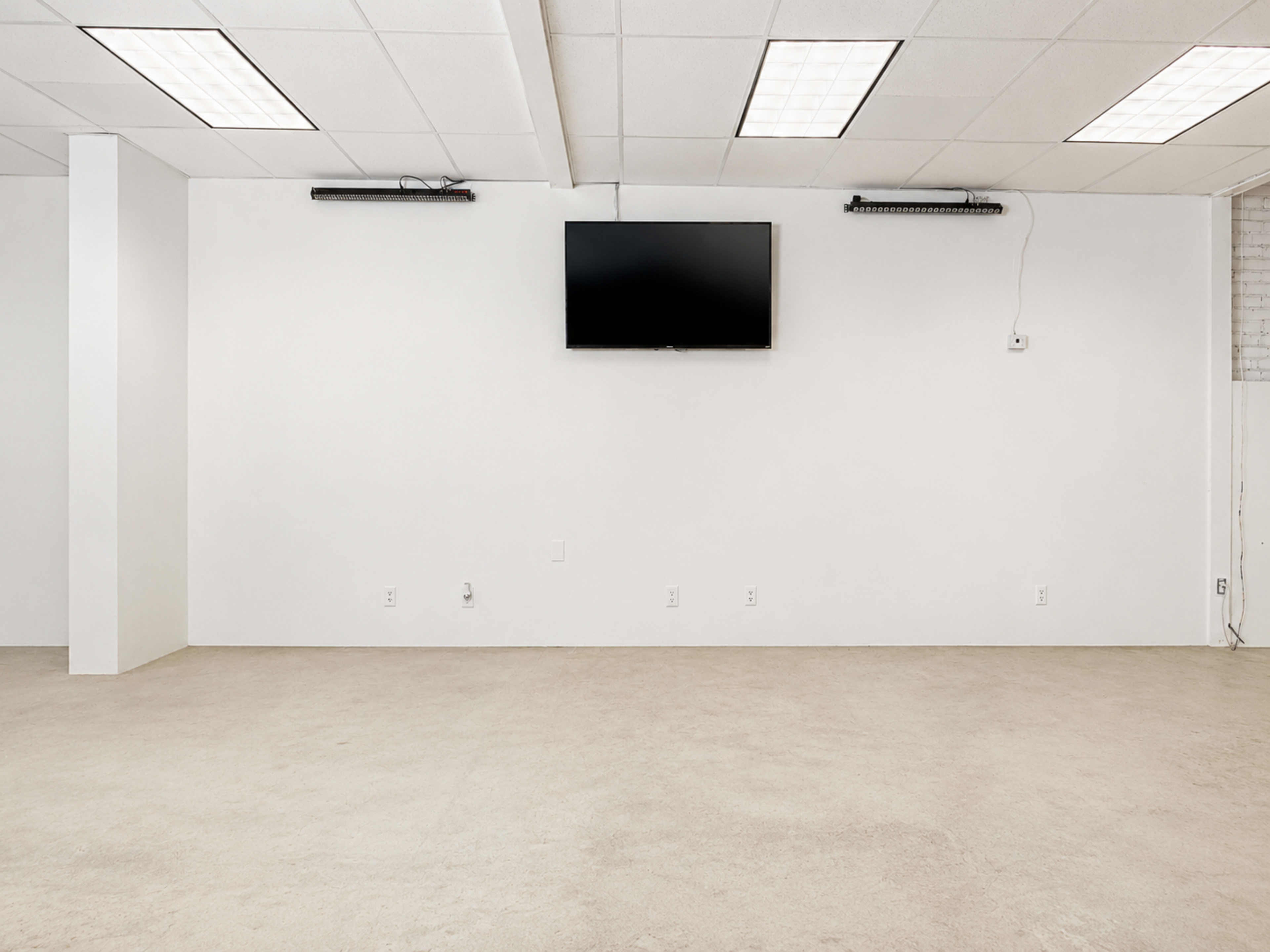 The image shows a minimally furnished room with a flat-screen TV mounted on a white wall and a smooth, bare floor.