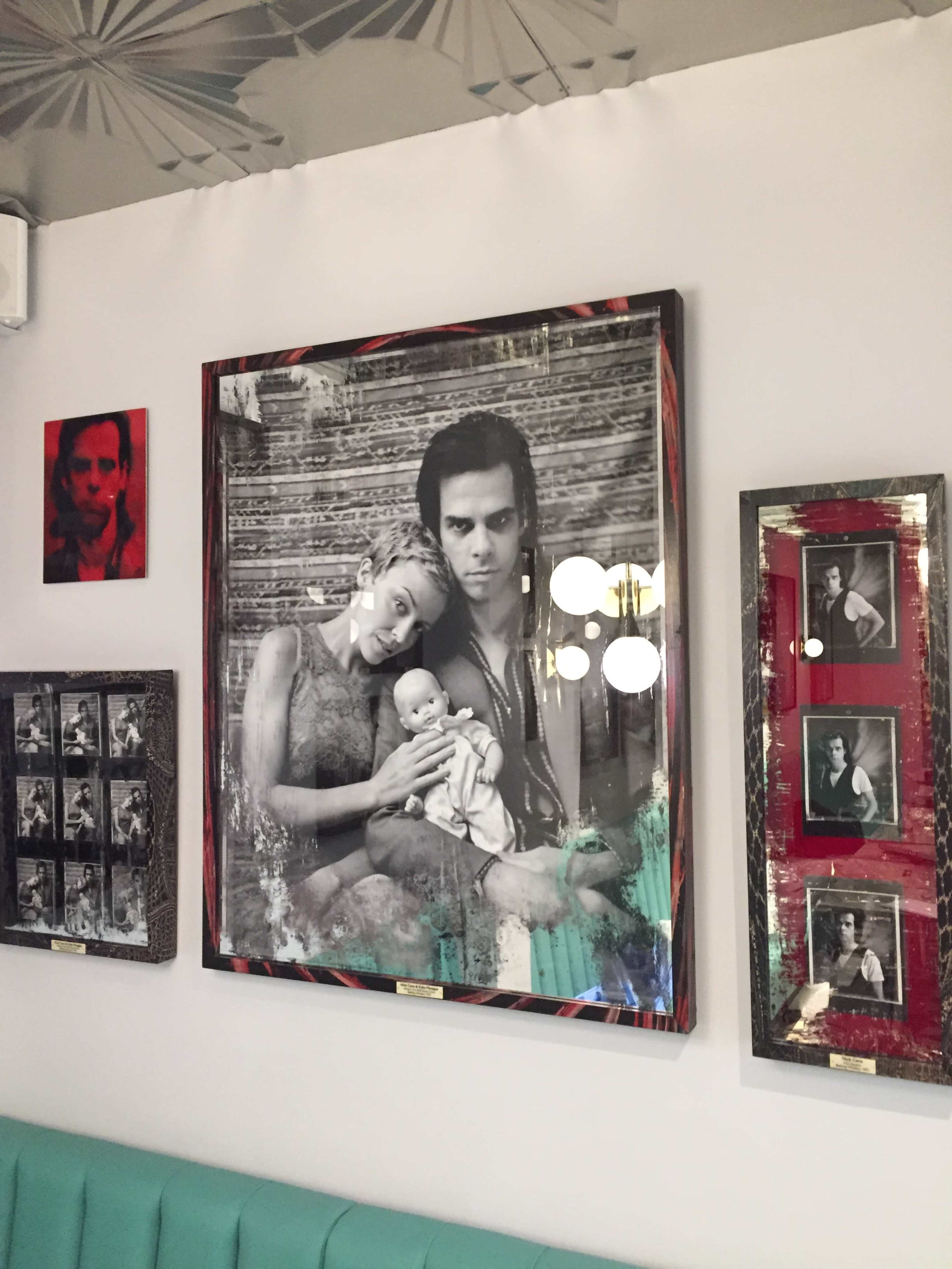 A wall featuring various framed black-and-white photographs, including a large portrait of a couple holding a baby and a smaller portrait of a man on the side.