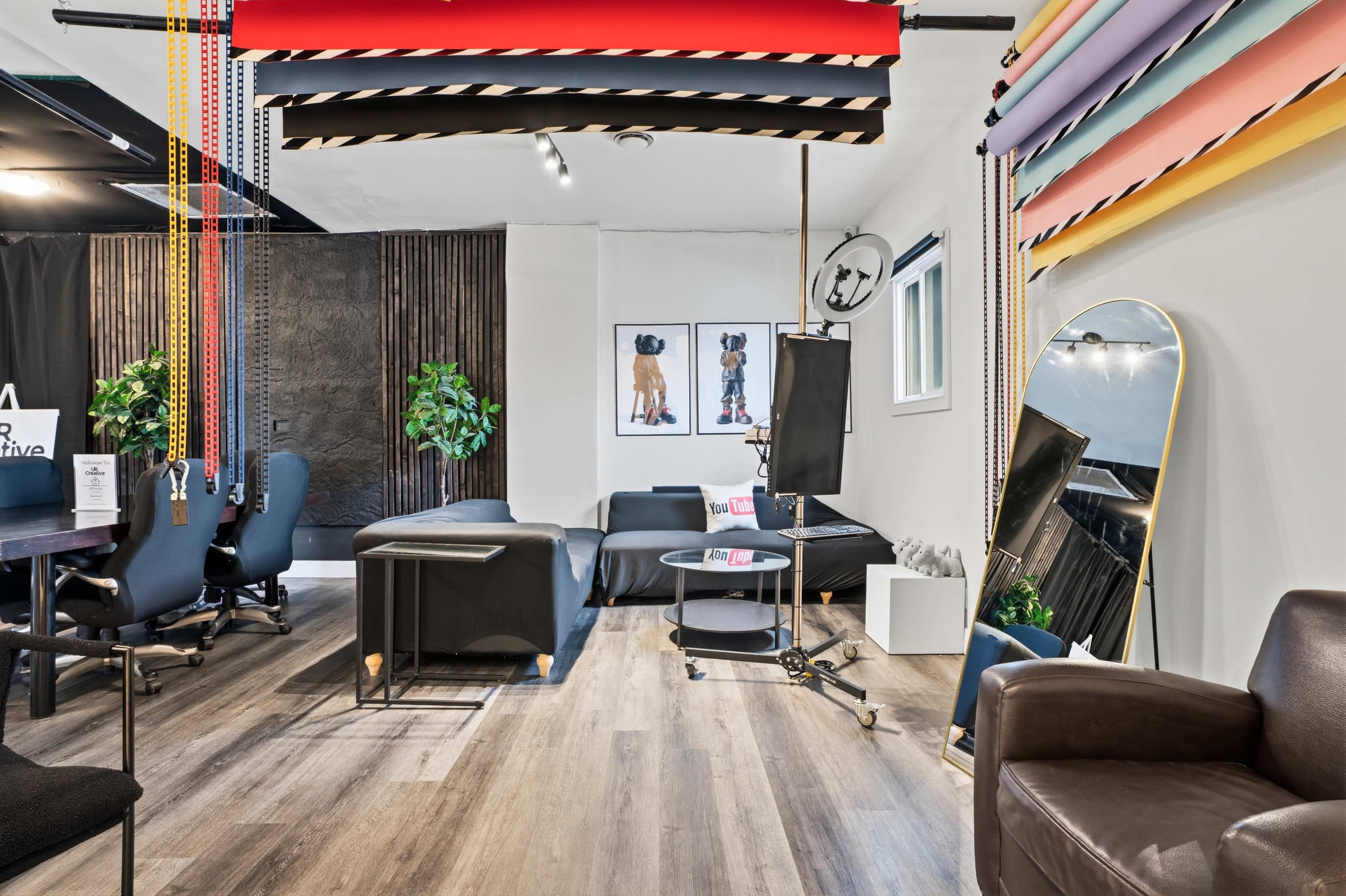 The image shows a modern workspace featuring a combination of office seating, a lounging area, and colorful decorative elements on the walls.
