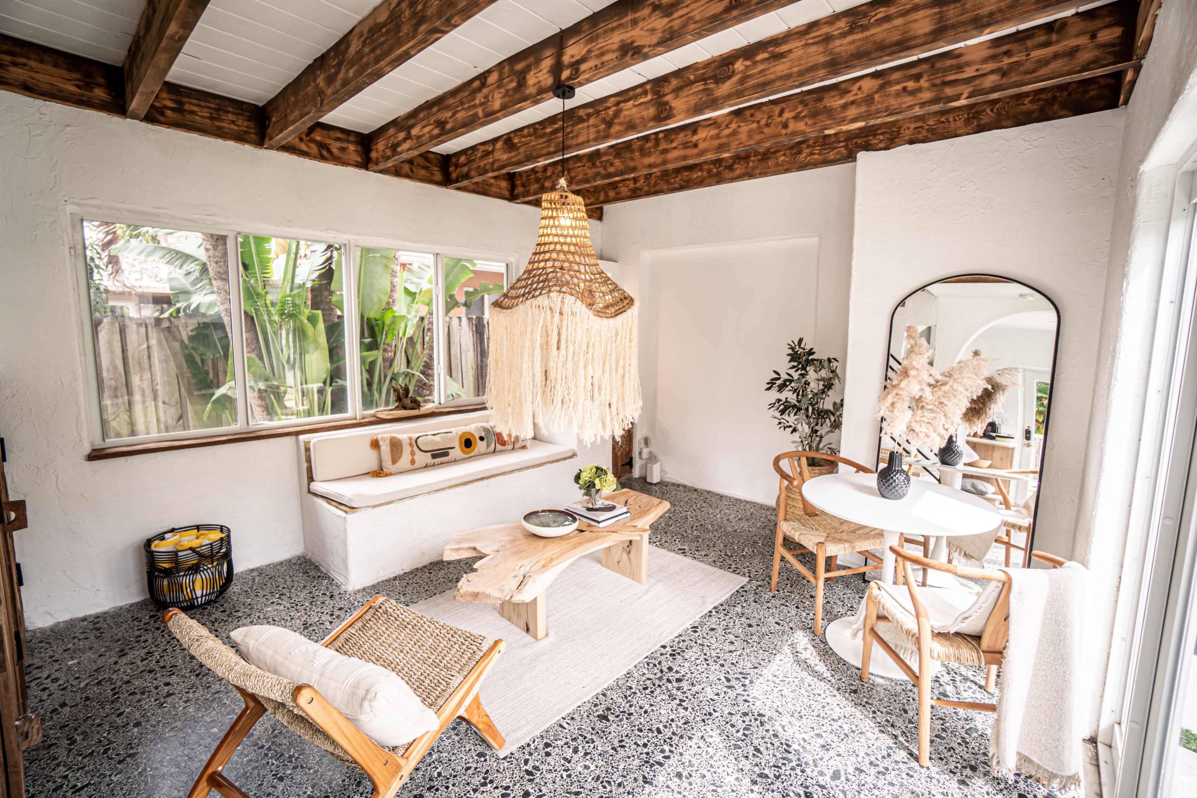 The image shows a bright, airy living space featuring a woven pendant light, a wooden coffee table, and a small dining area with two chairs.