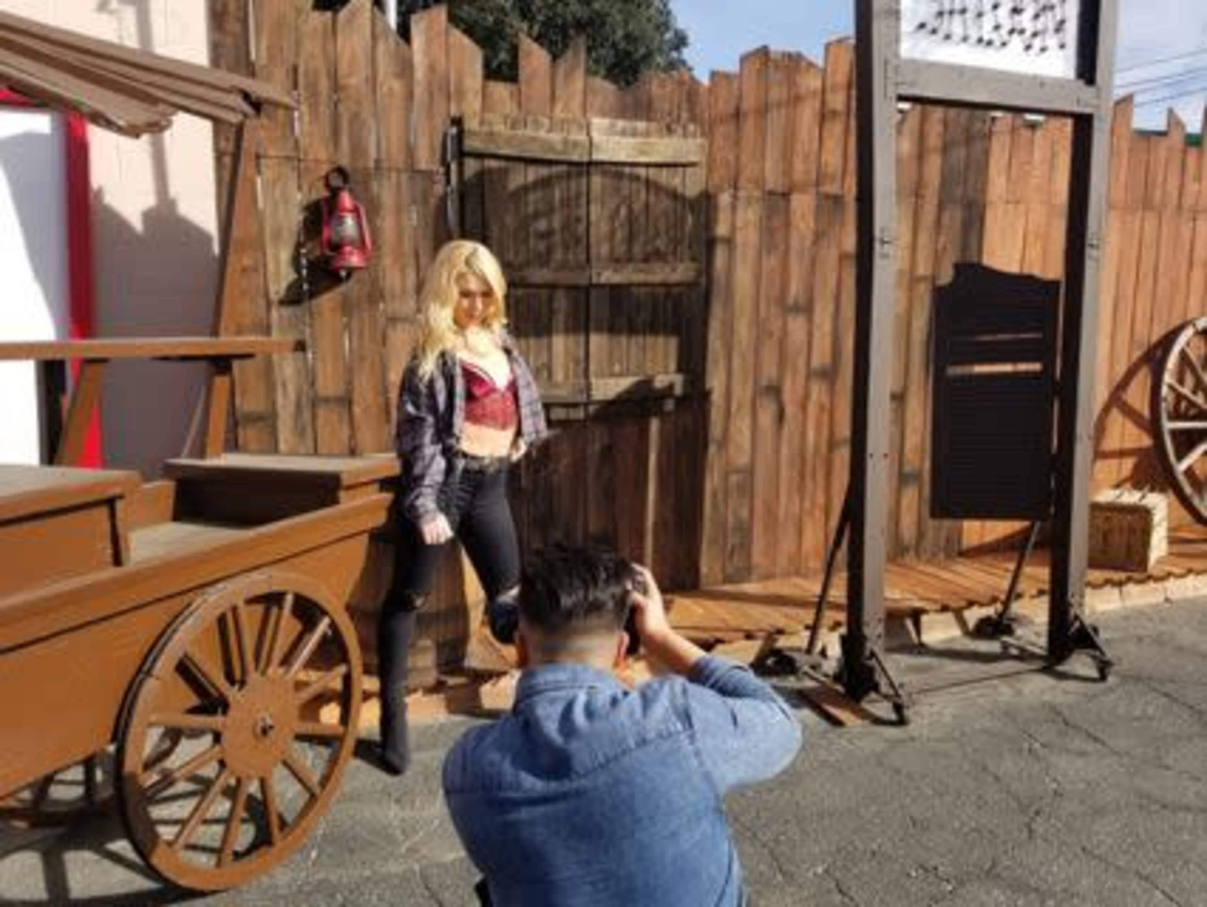 A photographer captures an image of a model posing in front of a wooden backdrop with various rustic features.