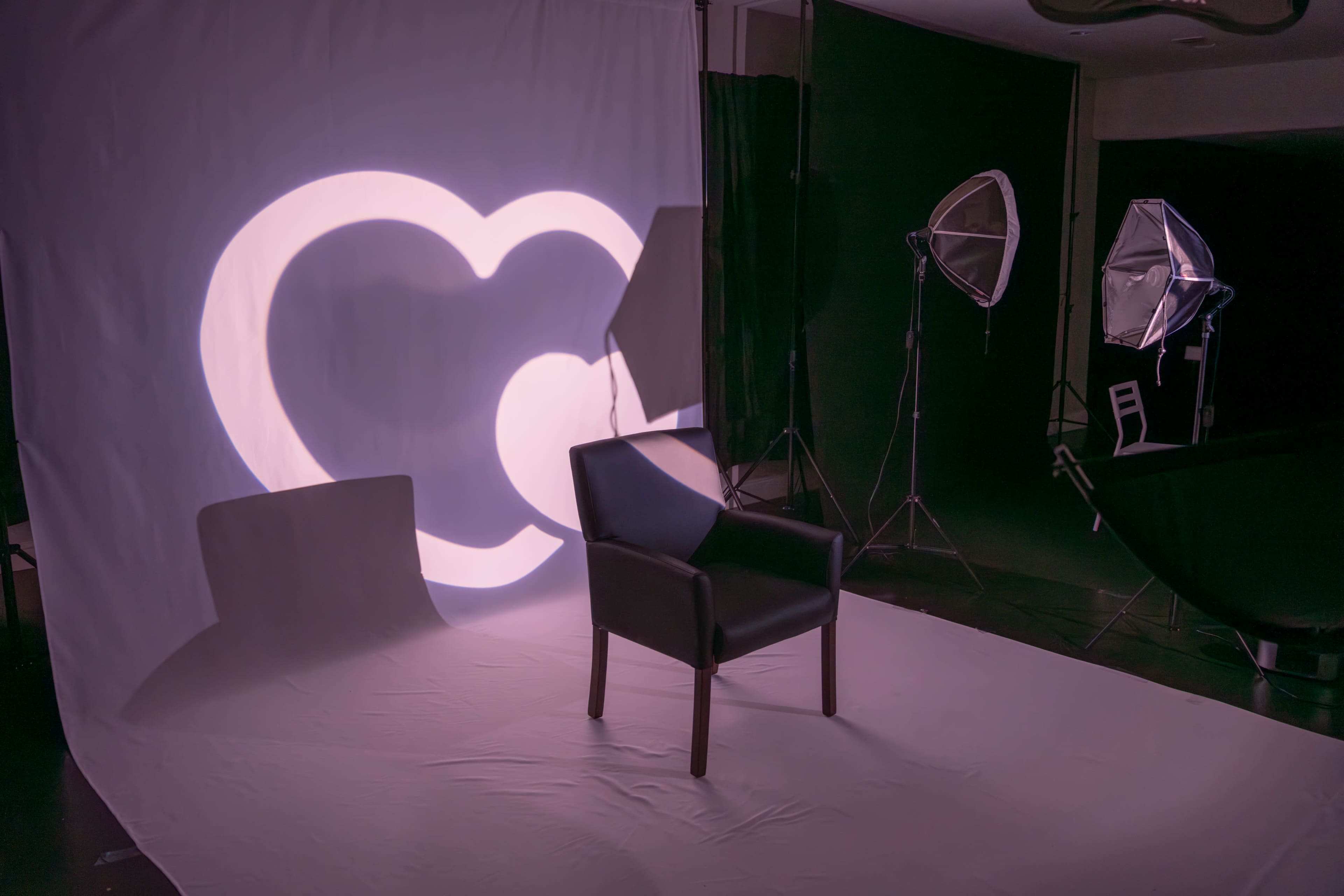 A black chair sits on a white backdrop illuminated by a heart-shaped light pattern.