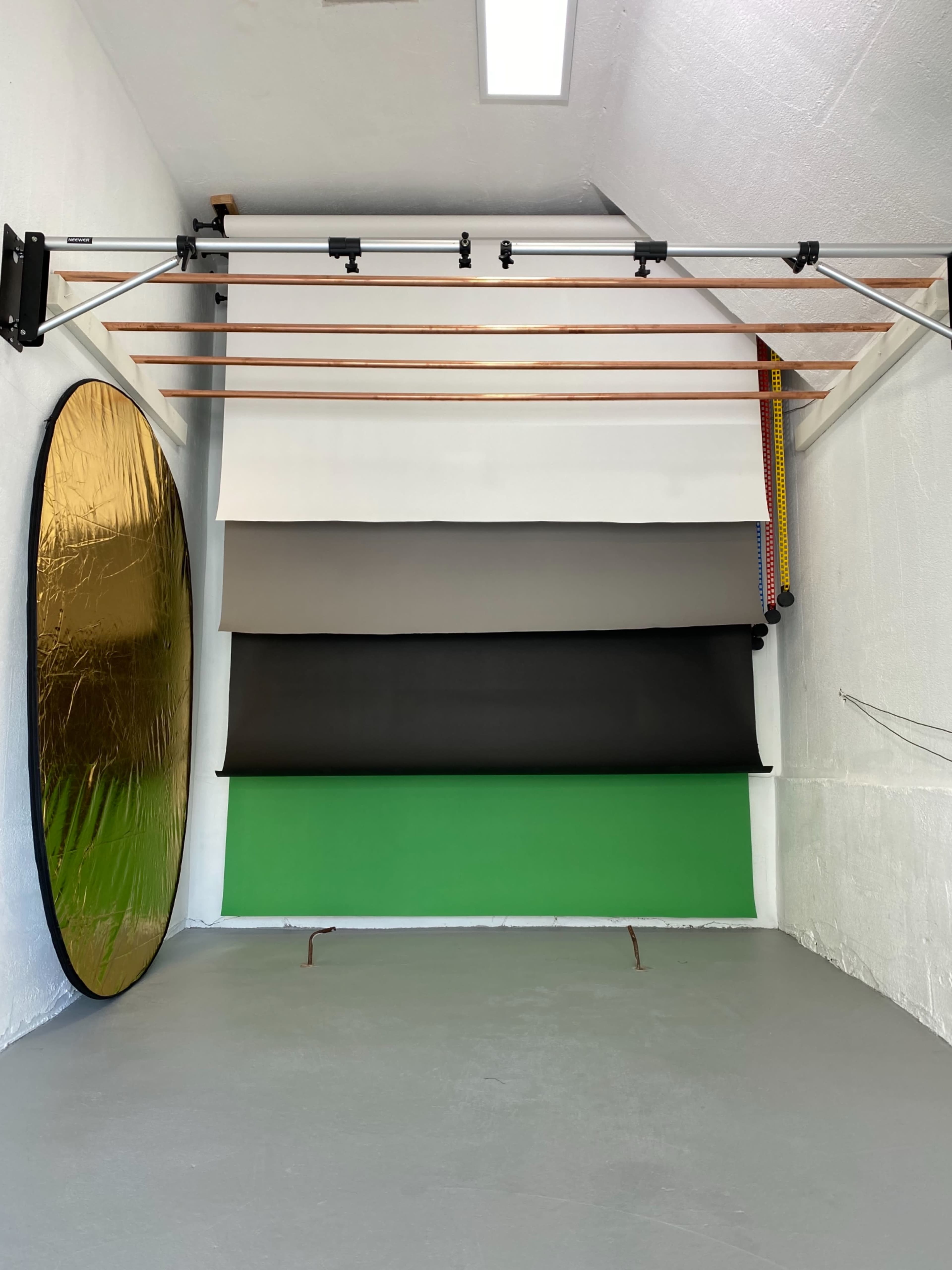 A photography studio with a selection of backdrops, including green, black, gray, and gold, arranged against a white wall.