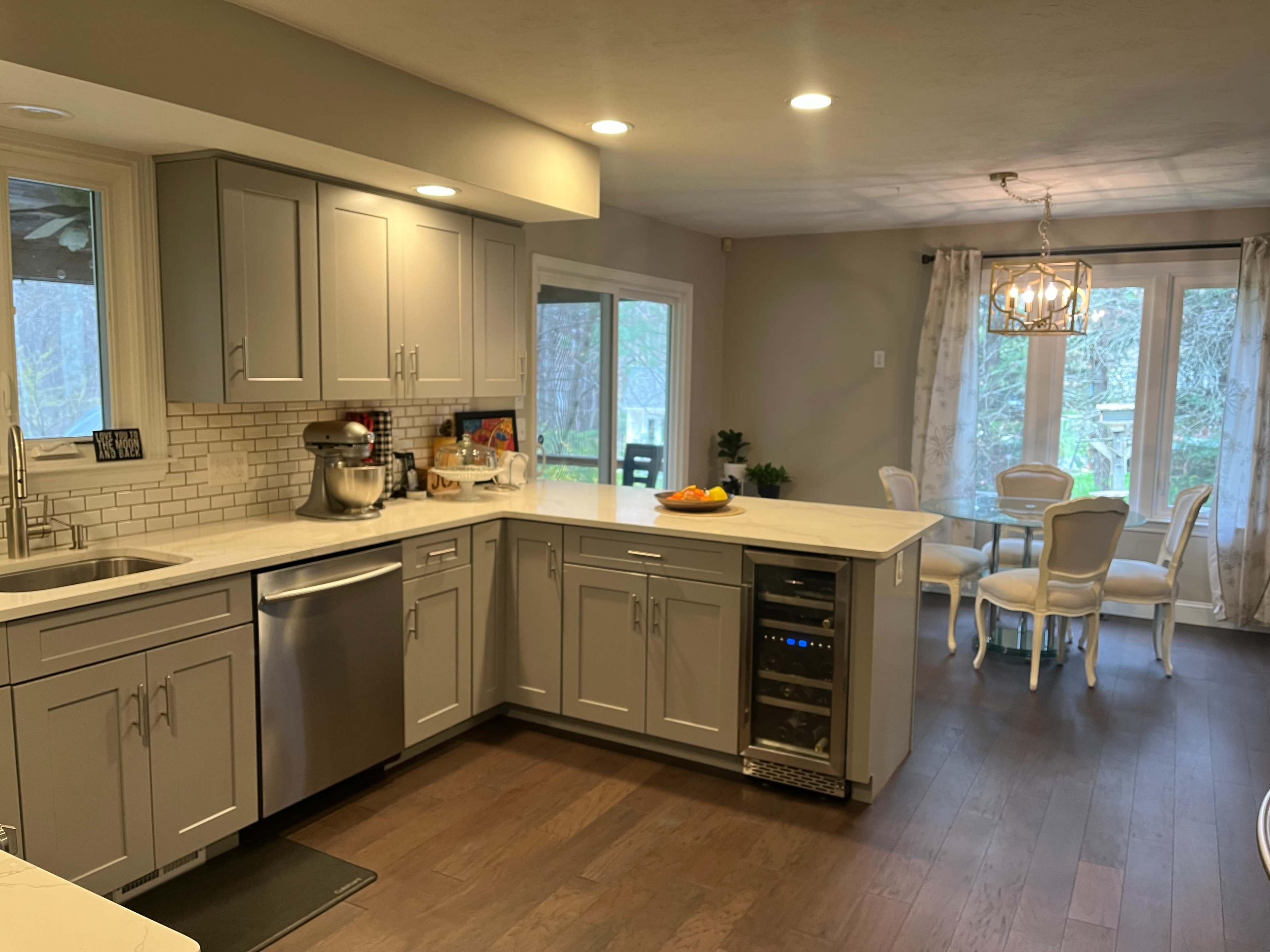 A spacious kitchen with gray cabinets, a stainless steel sink, and a countertop next to a small dining area featuring a round table and chairs.