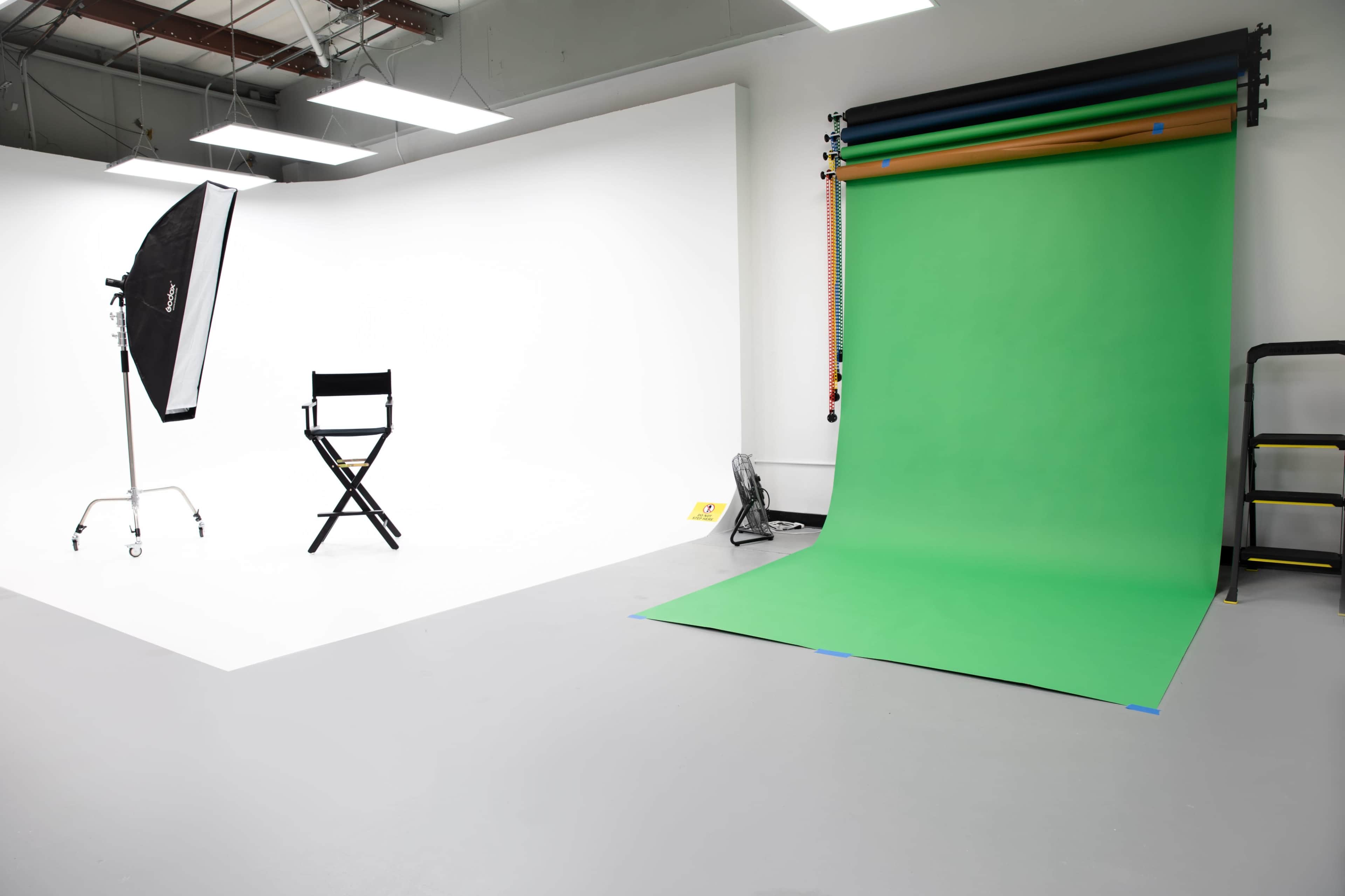 A photography studio with a green backdrop, a director's chair, and lighting equipment.
