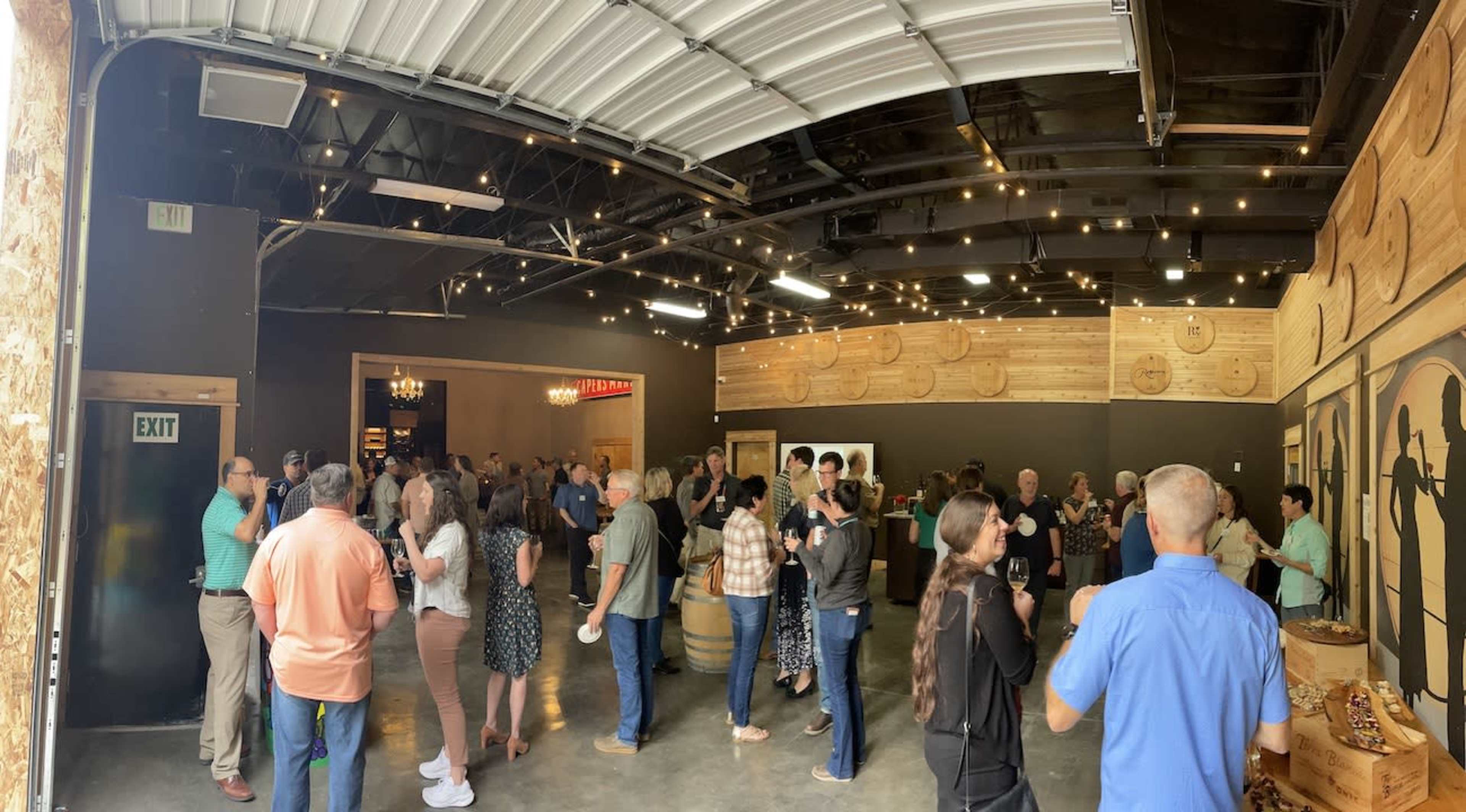 A crowd of people mingles inside a spacious venue featuring wooden accents and decorative lighting.