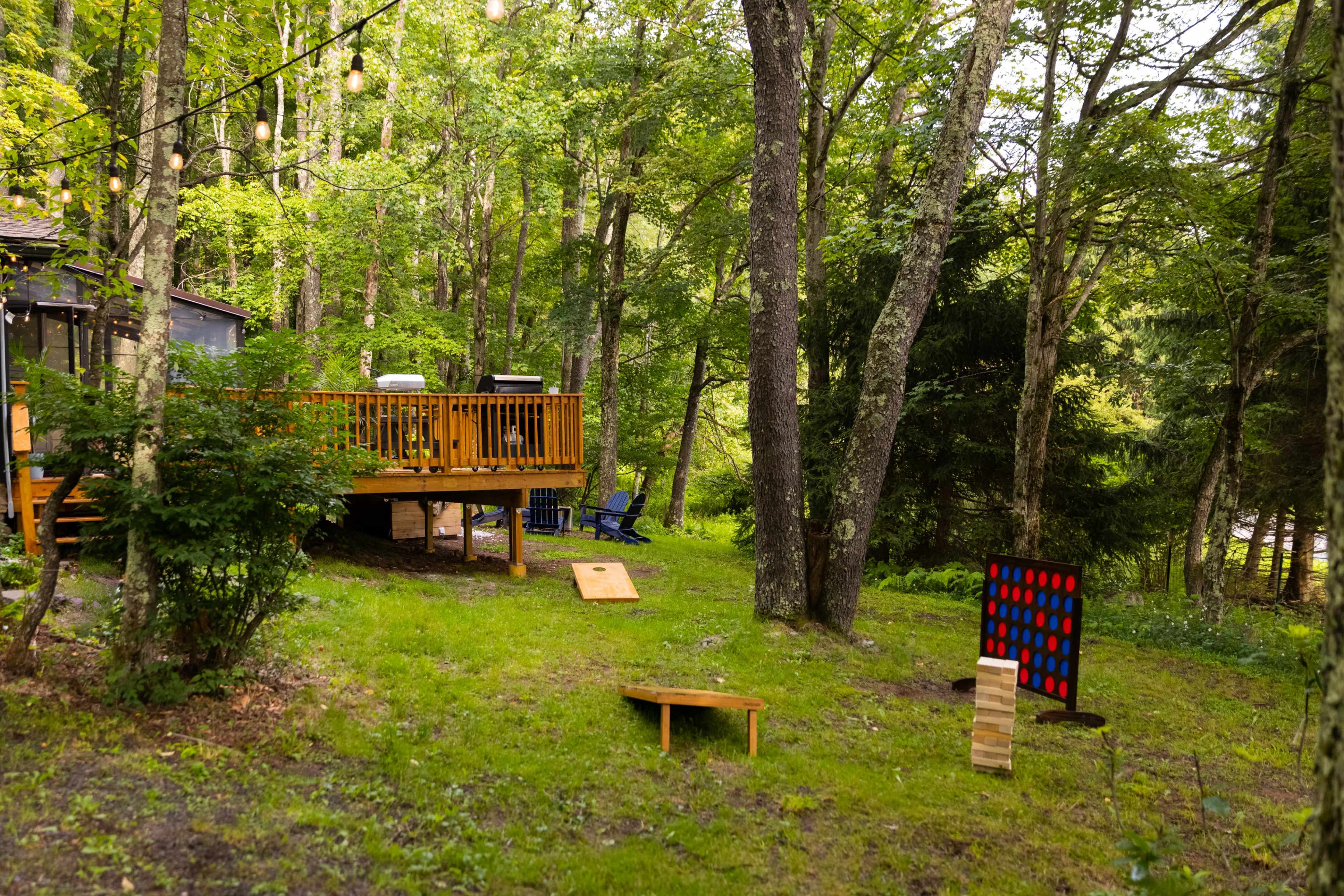 A wooden deck surrounded by trees features outdoor seating and games on the lawn.