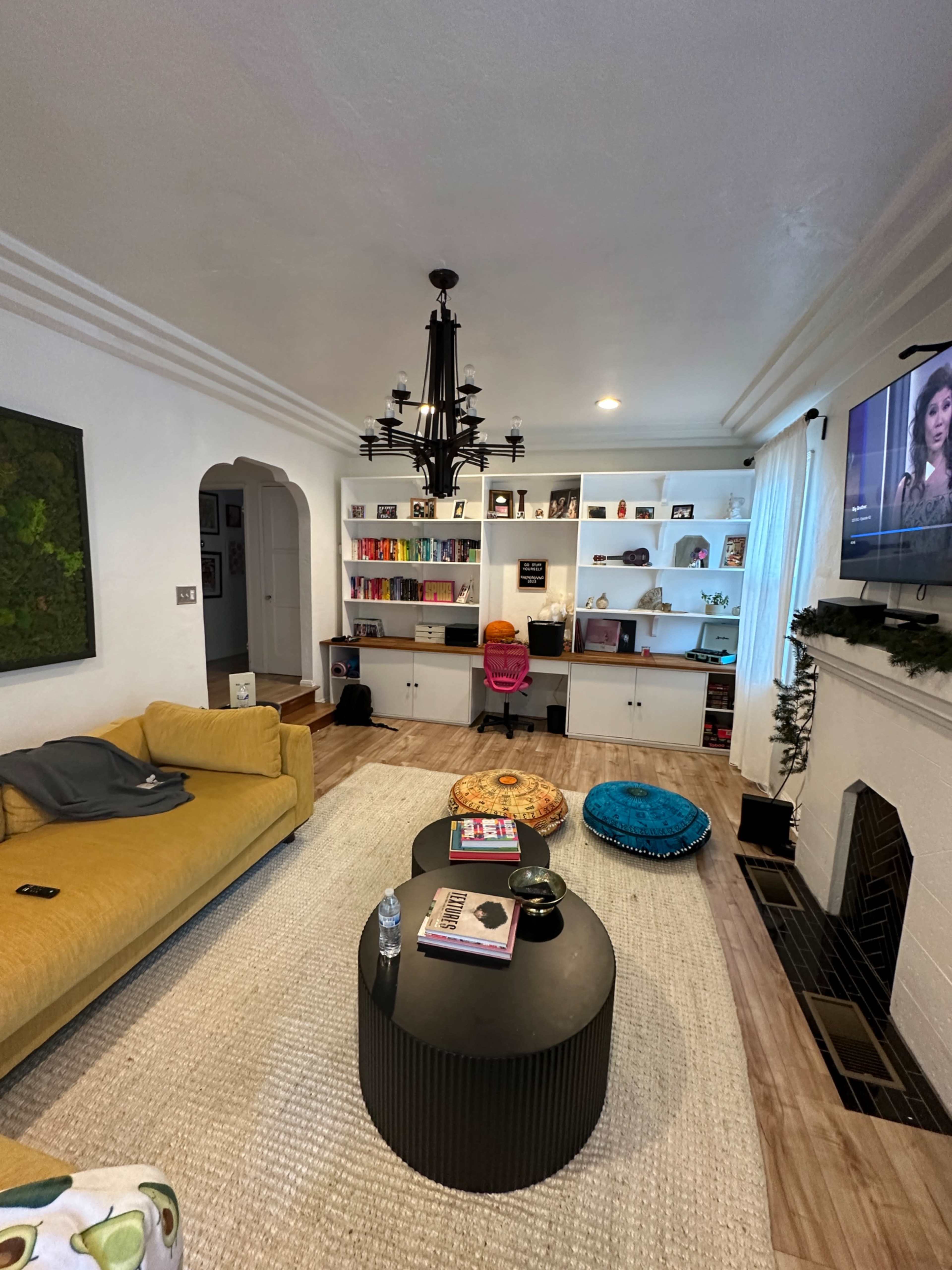 A living room with a yellow sofa, a round coffee table in the center, and shelves filled with books and decorative items along the wall.