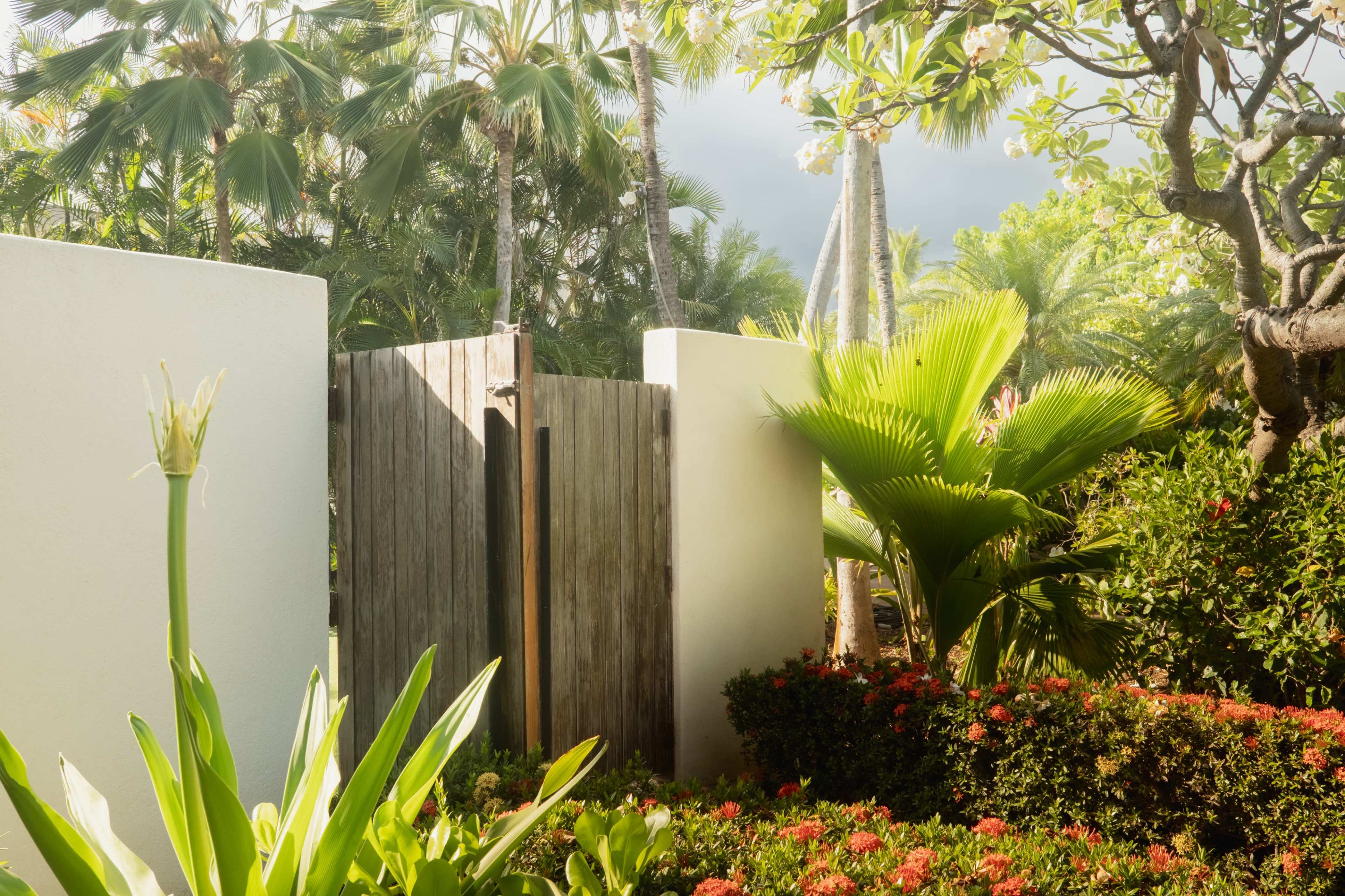 A wooden gate is framed by lush greenery and colorful flowers in a tropical garden.