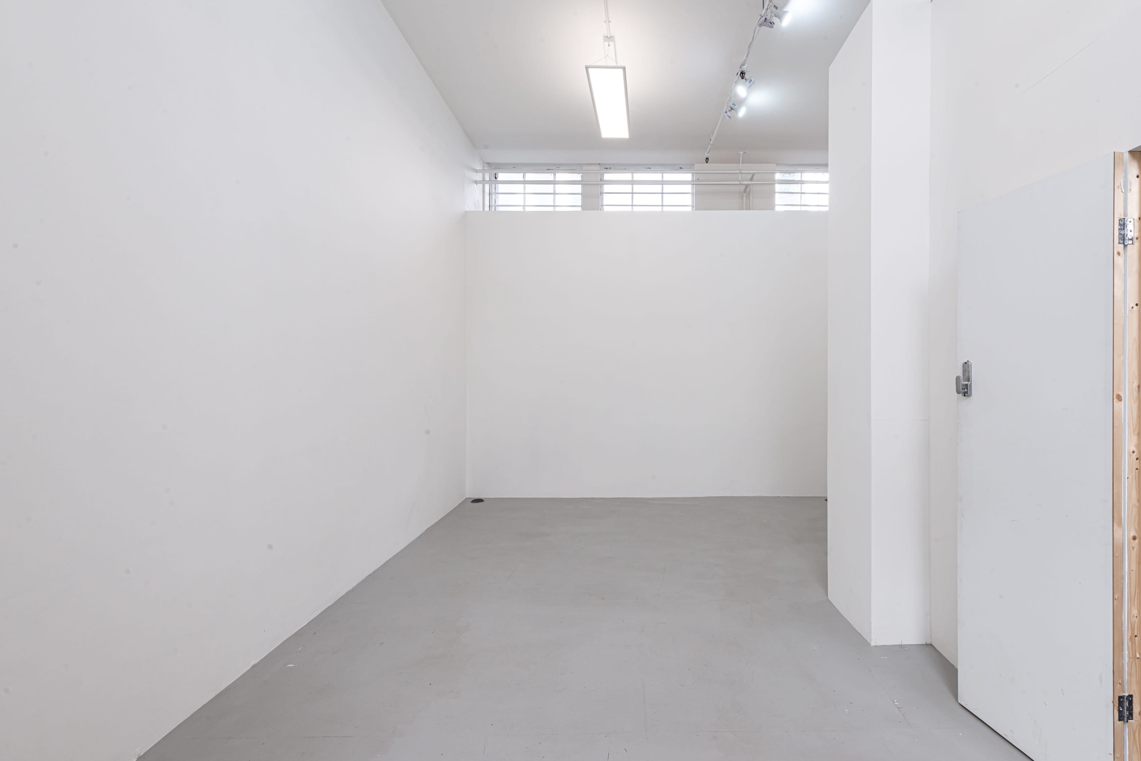 An empty, white-walled interior space with a concrete floor and a doorway on the right.