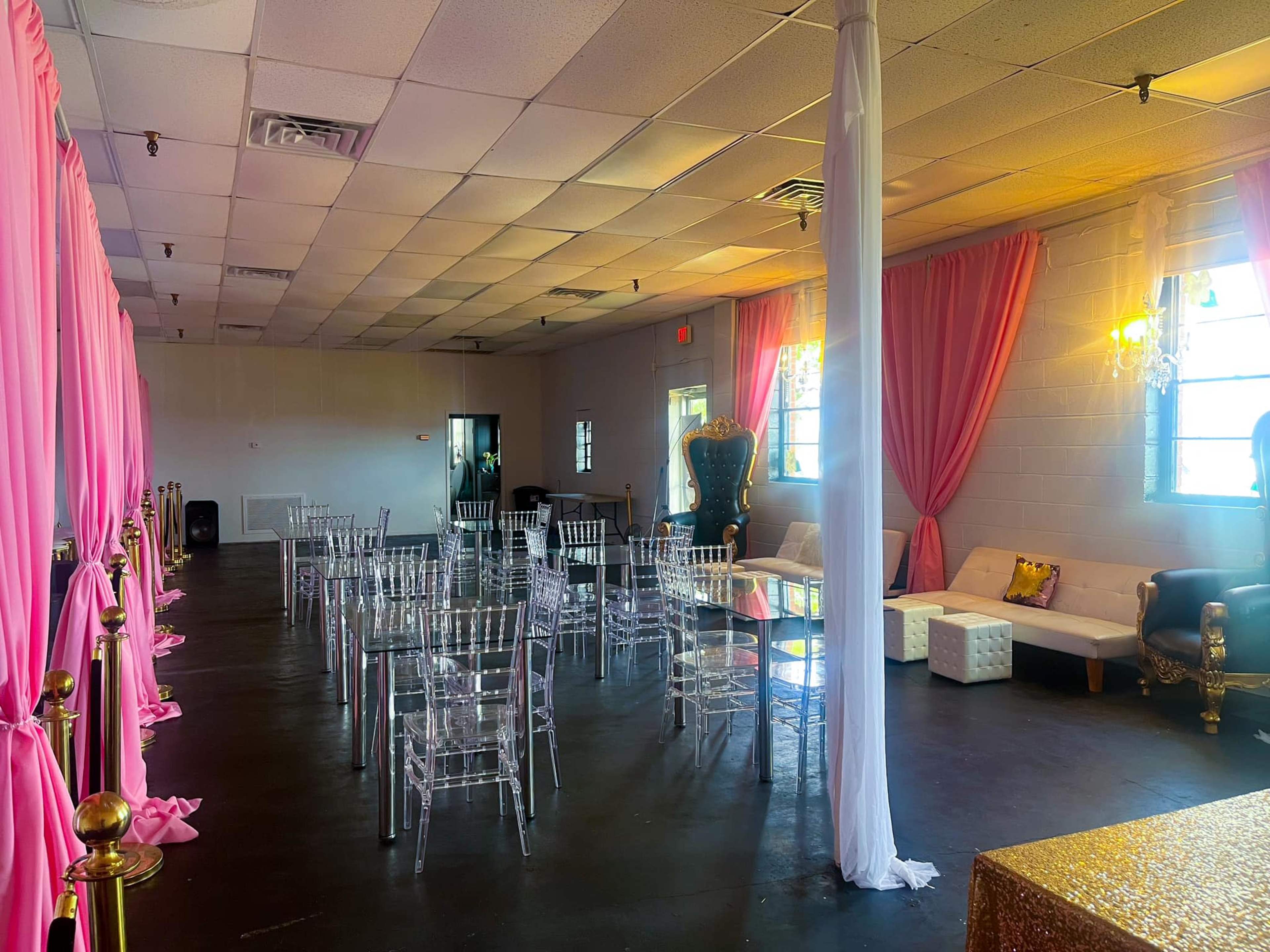 A spacious event venue featuring rows of transparent chairs, pink curtains, and a mix of lounge seating.