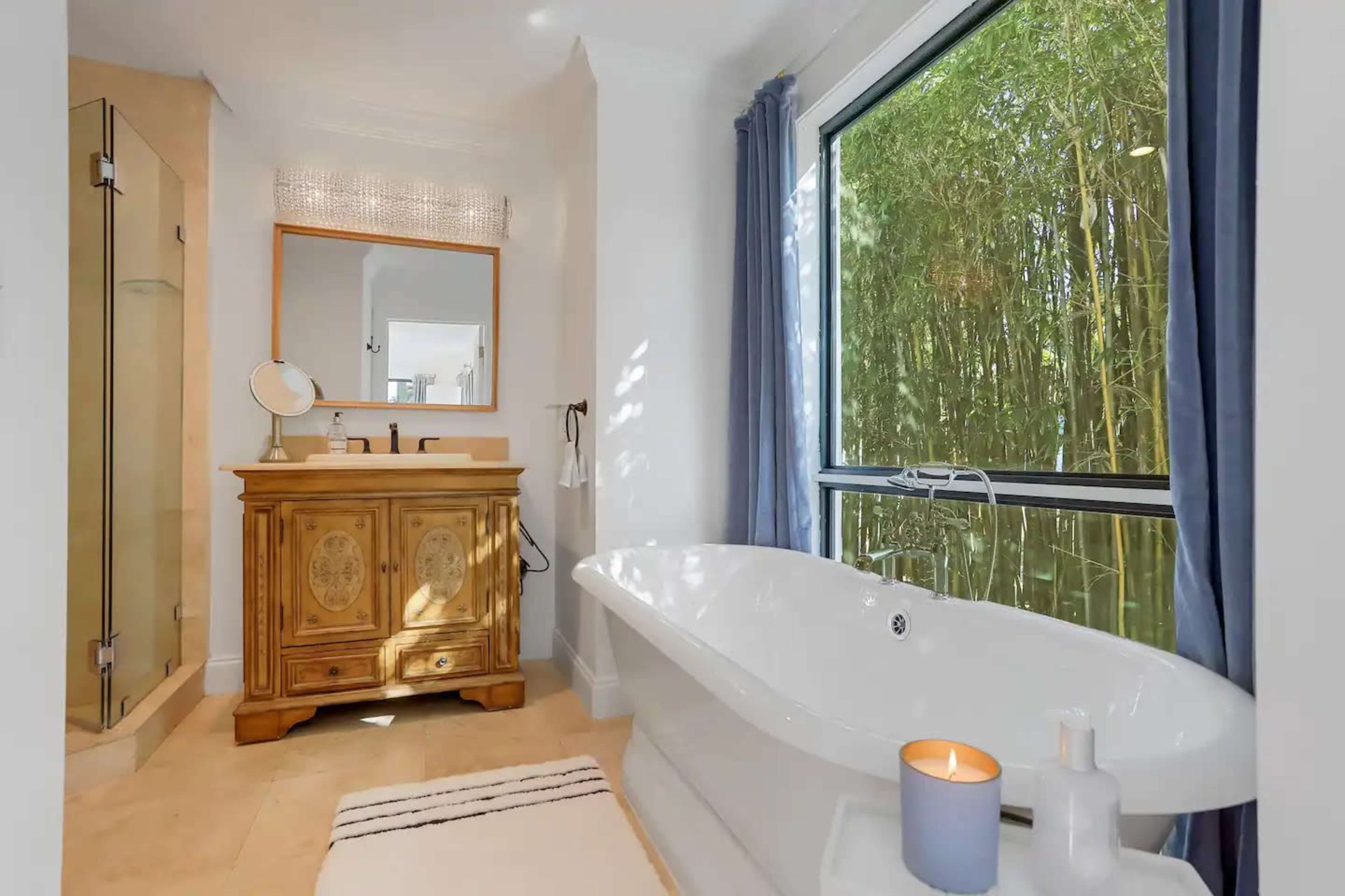 A bright bathroom featuring a freestanding bathtub, a wooden vanity, and large windows overlooking a bamboo grove.