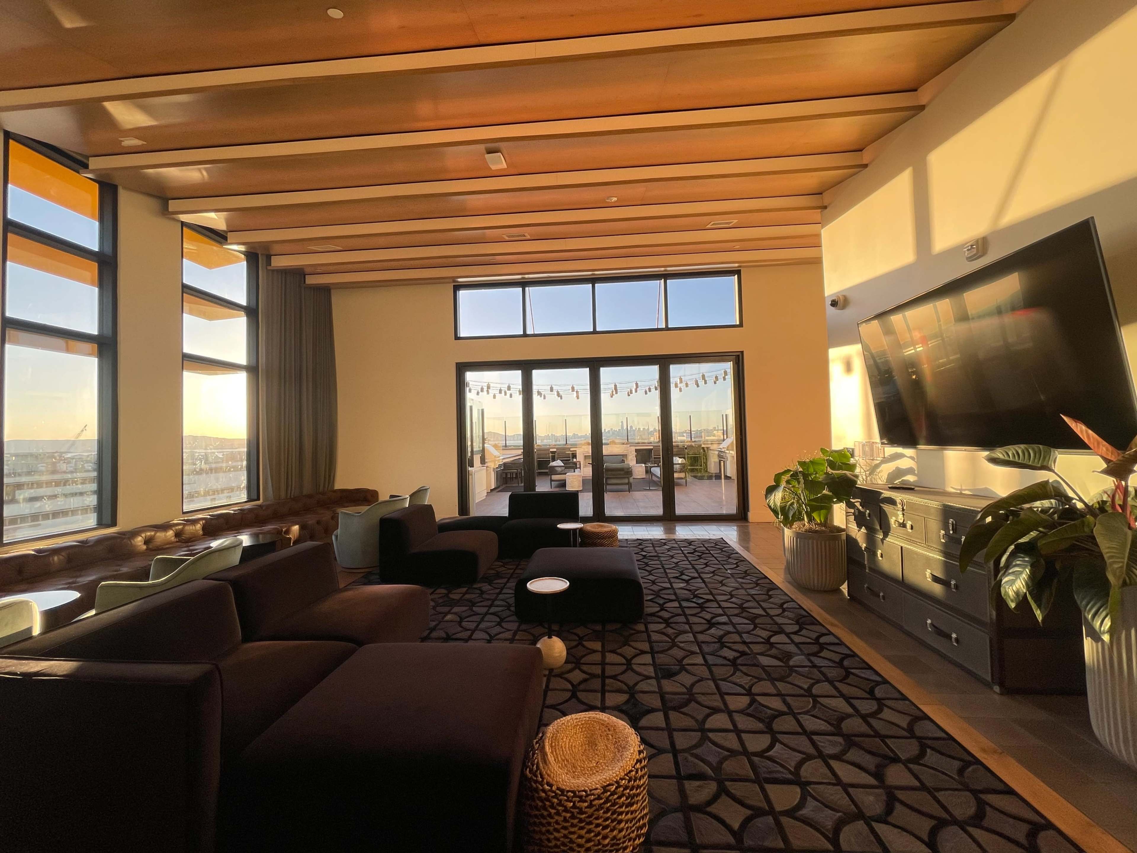 A modern lounge area with large windows, a sectional sofa, and a view of an outdoor space with string lights.