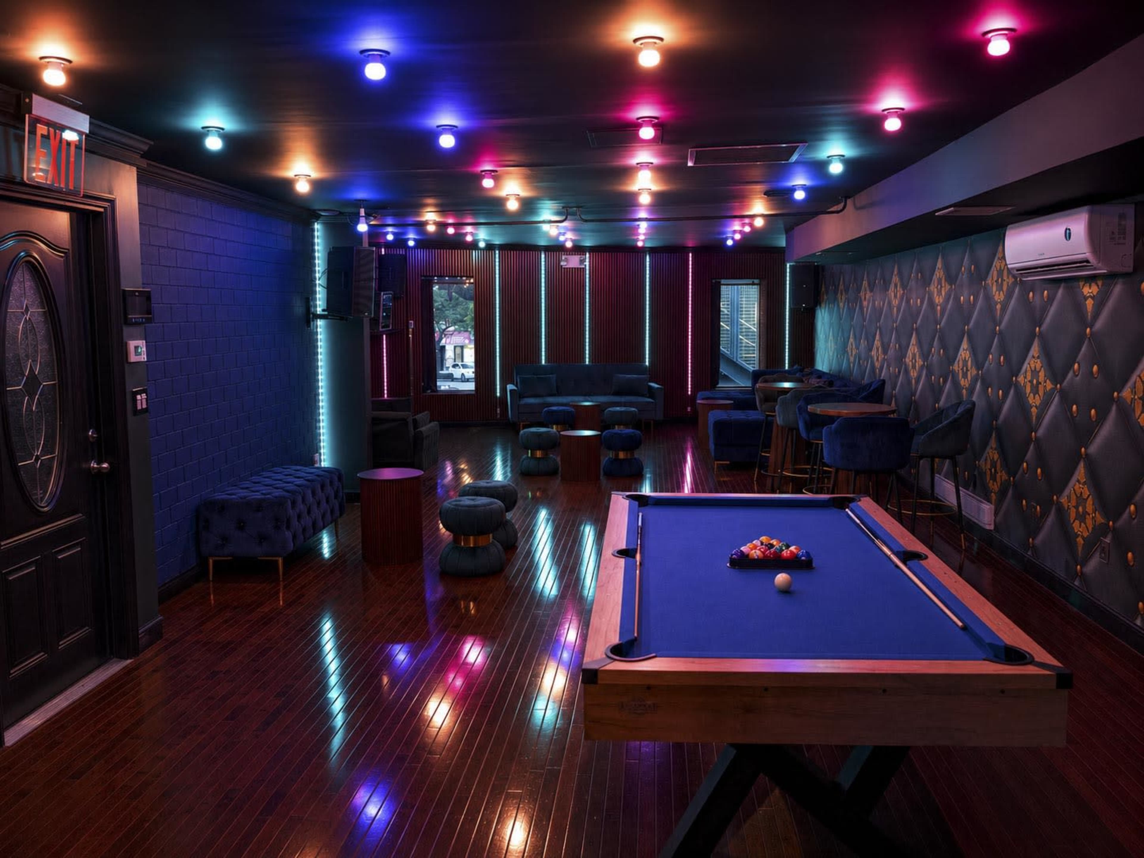 The image shows a stylish interior of a game room featuring a blue pool table, plush seating, and vibrant multicolored lighting.