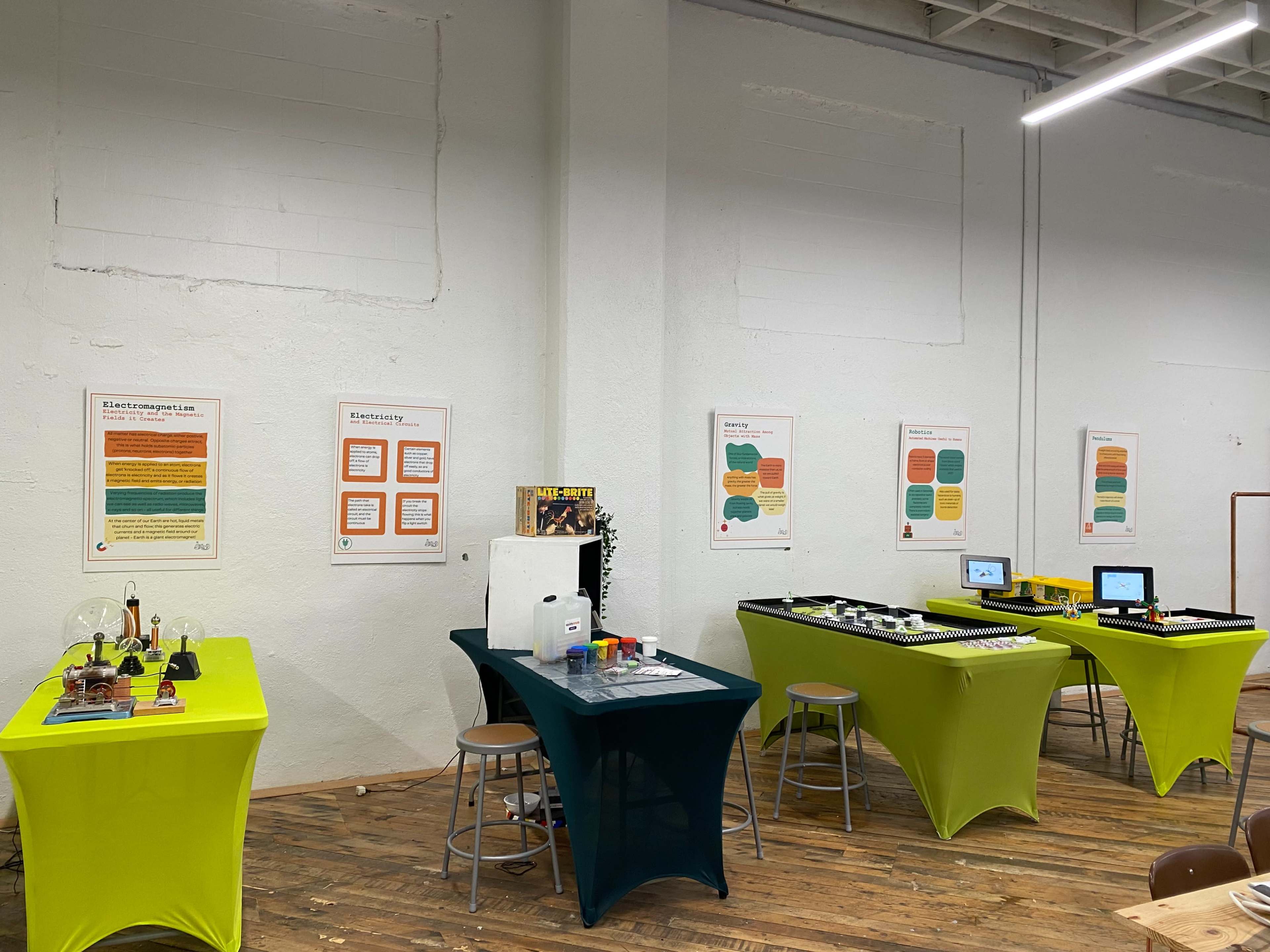 A spacious room with two distinct tables covered in colored cloths, displaying various scientific equipment and signage on the walls.
