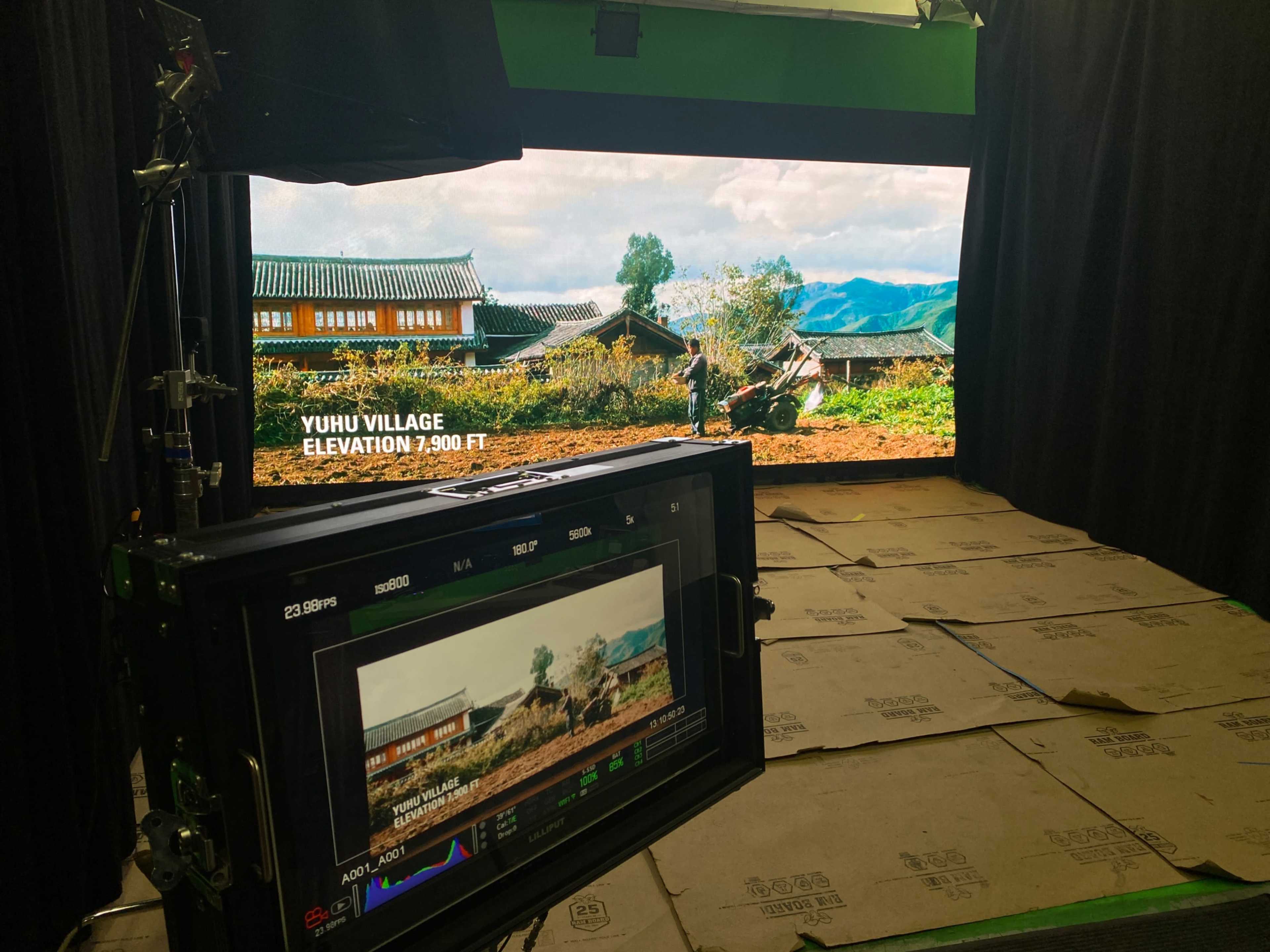 A video production setup features a display showing a scenic view of Yuhu Village with an elevation of 7,900 feet, while a monitor is positioned in the foreground.