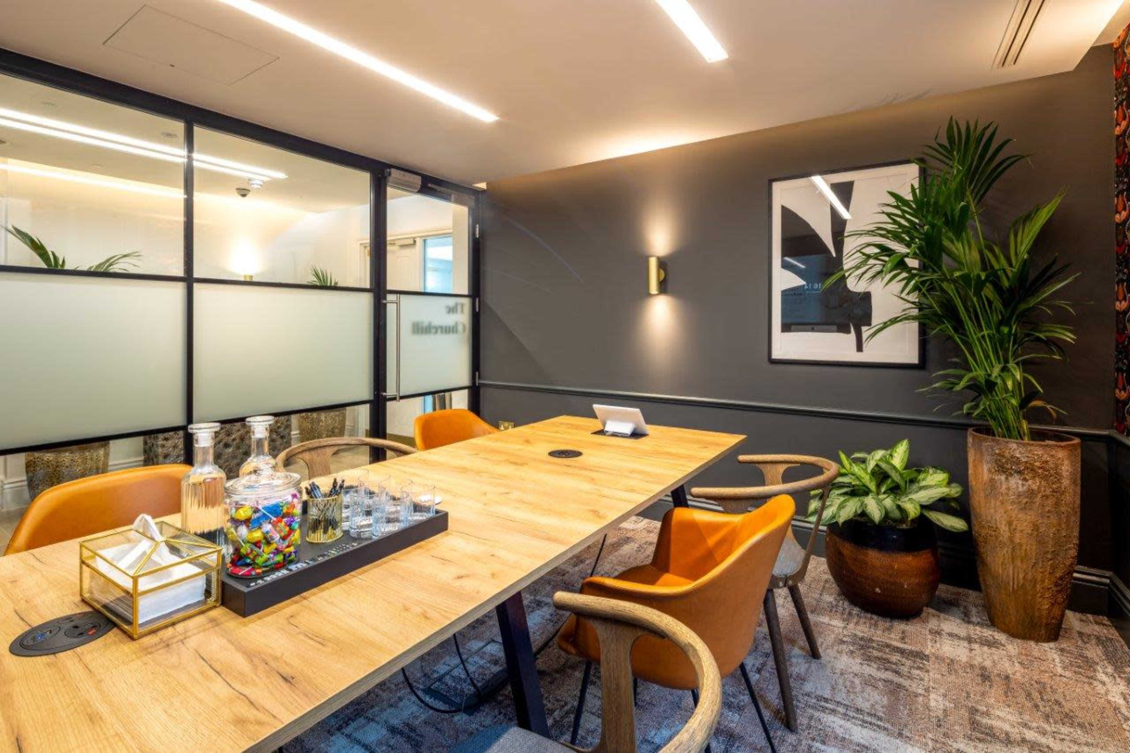 A modern conference room with a wooden table surrounded by orange chairs, a plant in the corner, and a decorative arrangement on the table.