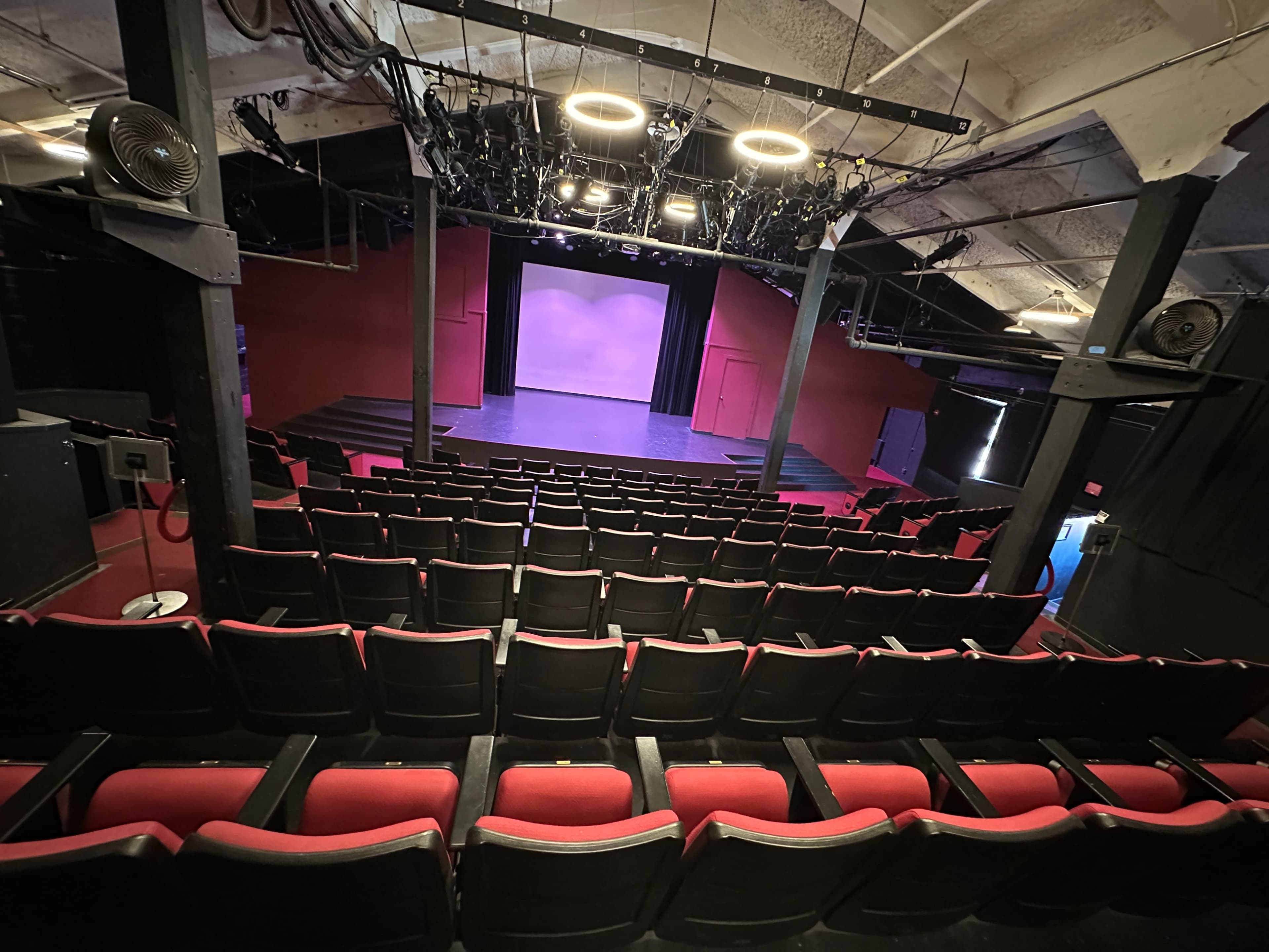 A theater with red seats facing a stage that is illuminated by overhead lights and has a purple backdrop.