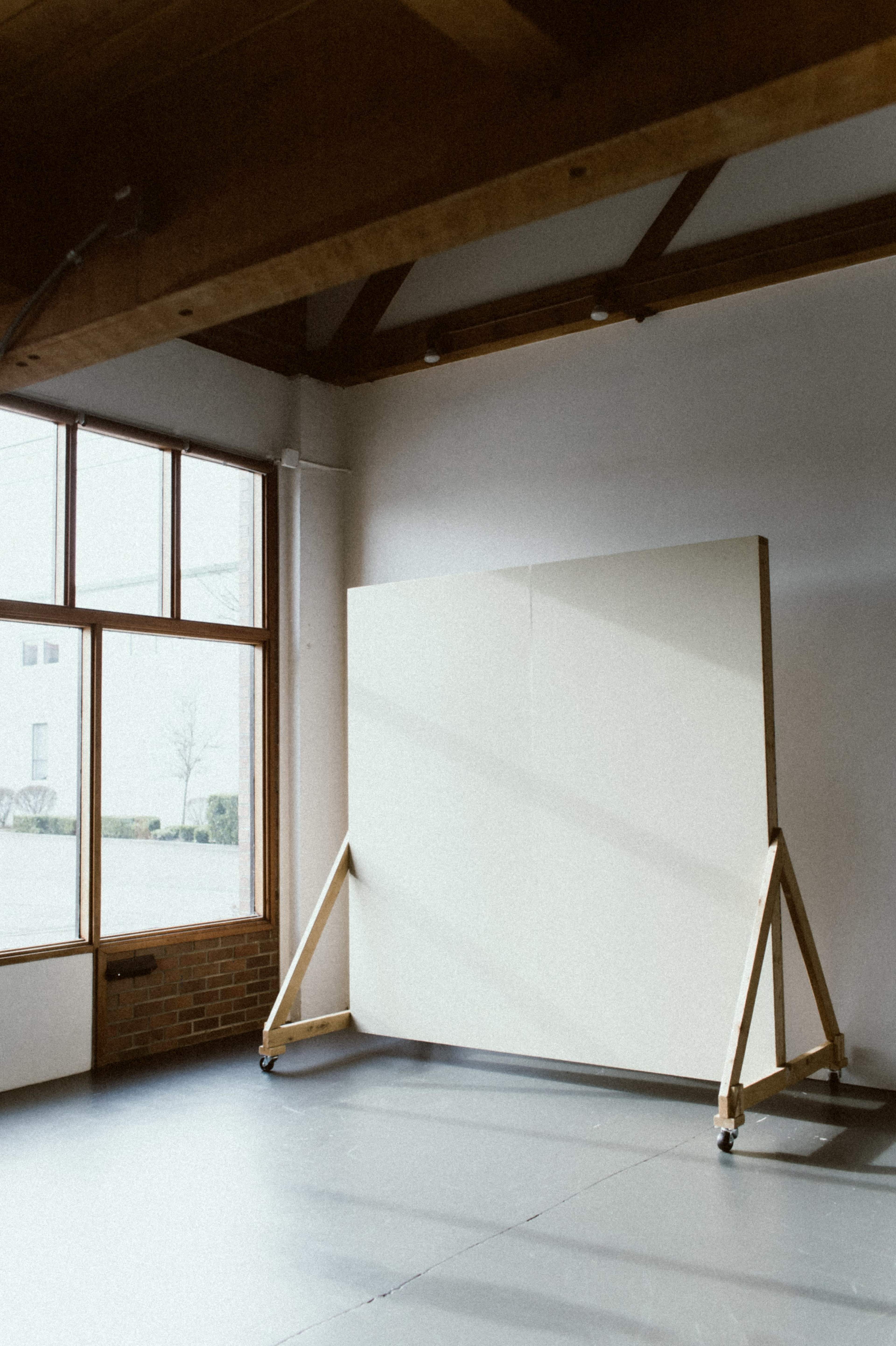 A spacious room with large windows and a blank canvas mounted on a wooden easel.