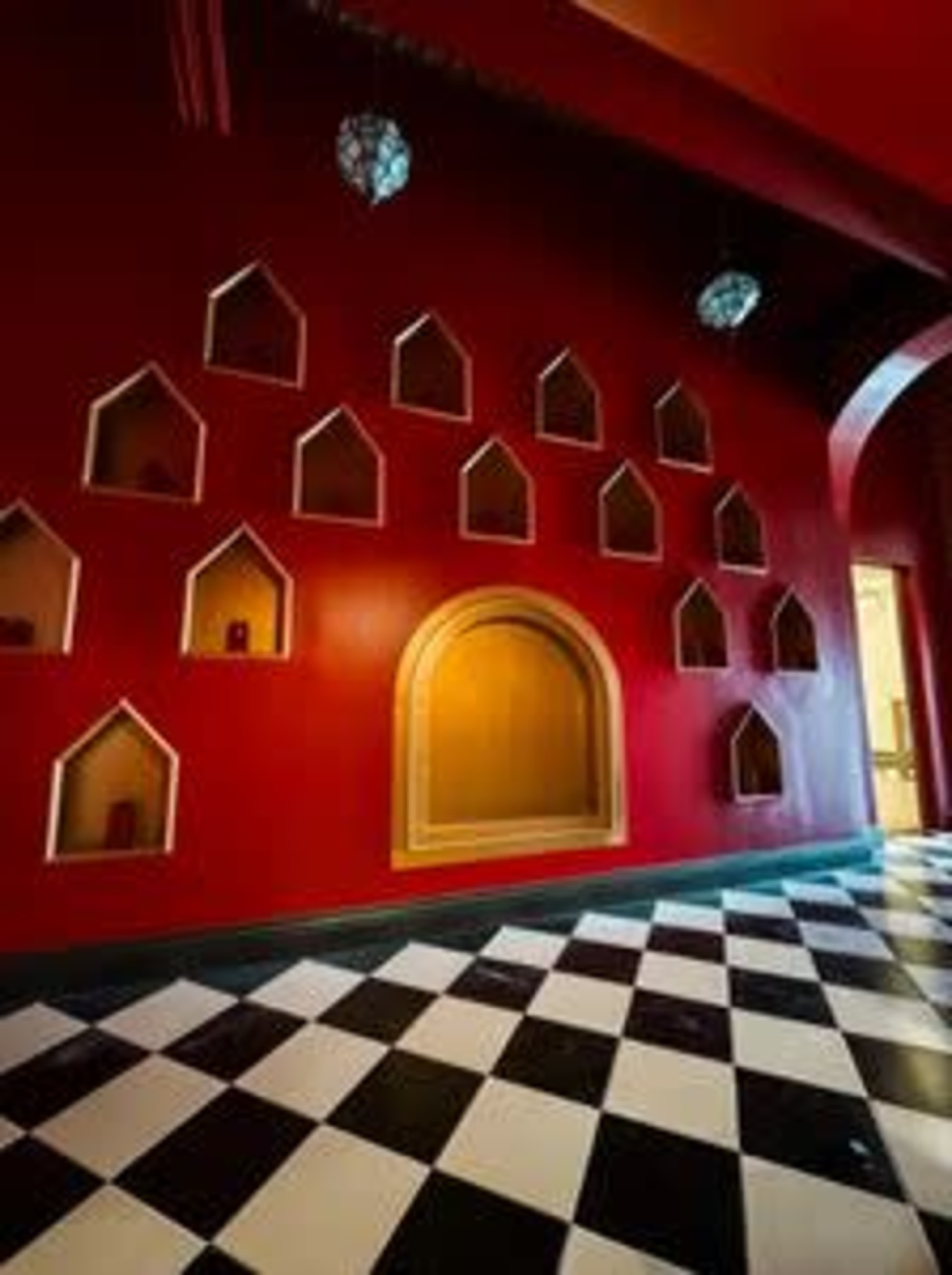 A red wall with multiple decorative alcoves shaped like small houses, adjacent to a checkerboard black and white floor.