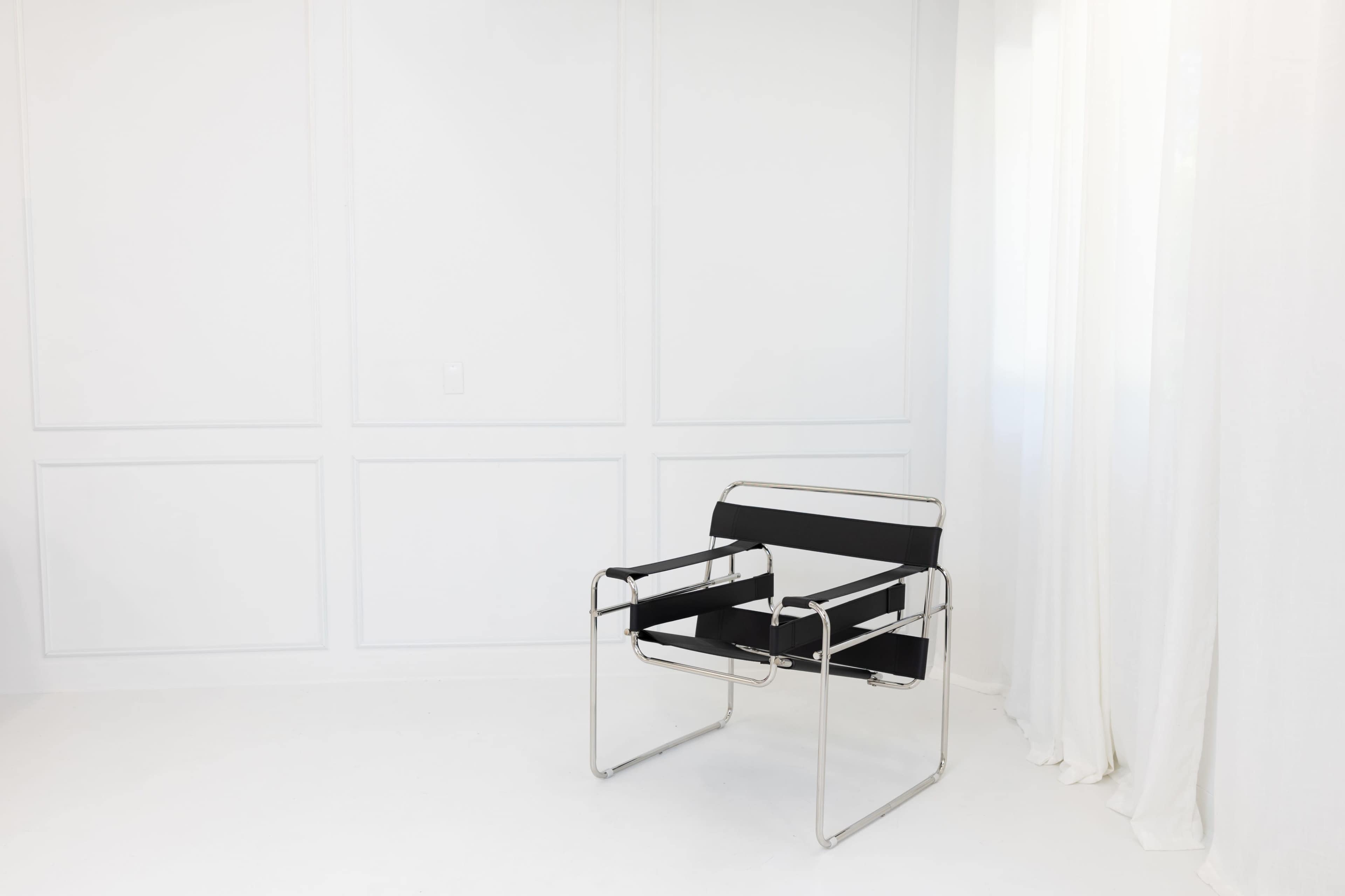 A modern black chair with a chrome frame is placed against a white wall in a bright, minimalist room.