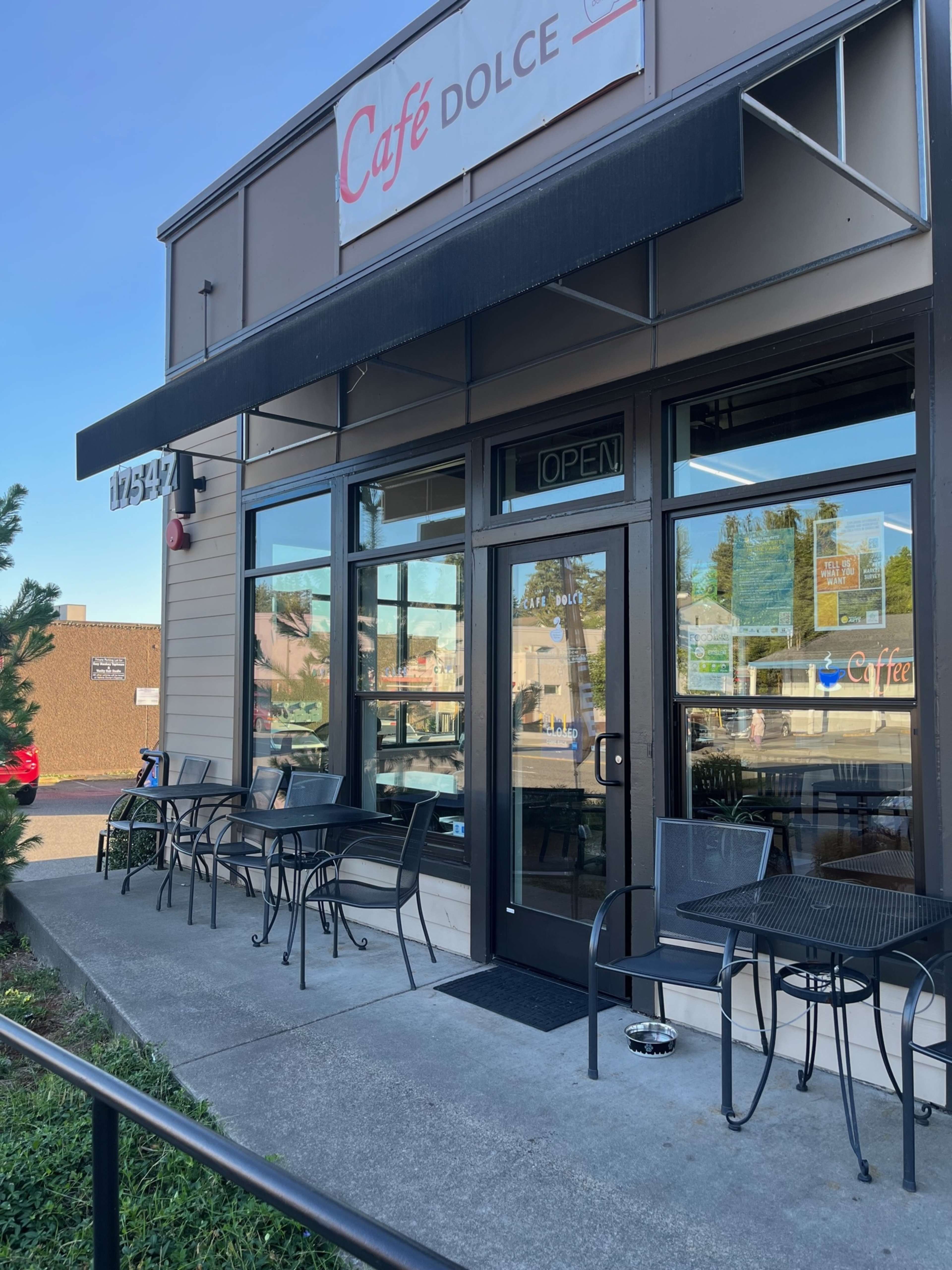 The entrance of Café Dolce, featuring a black awning, glass doors, and several outdoor tables along the sidewalk.