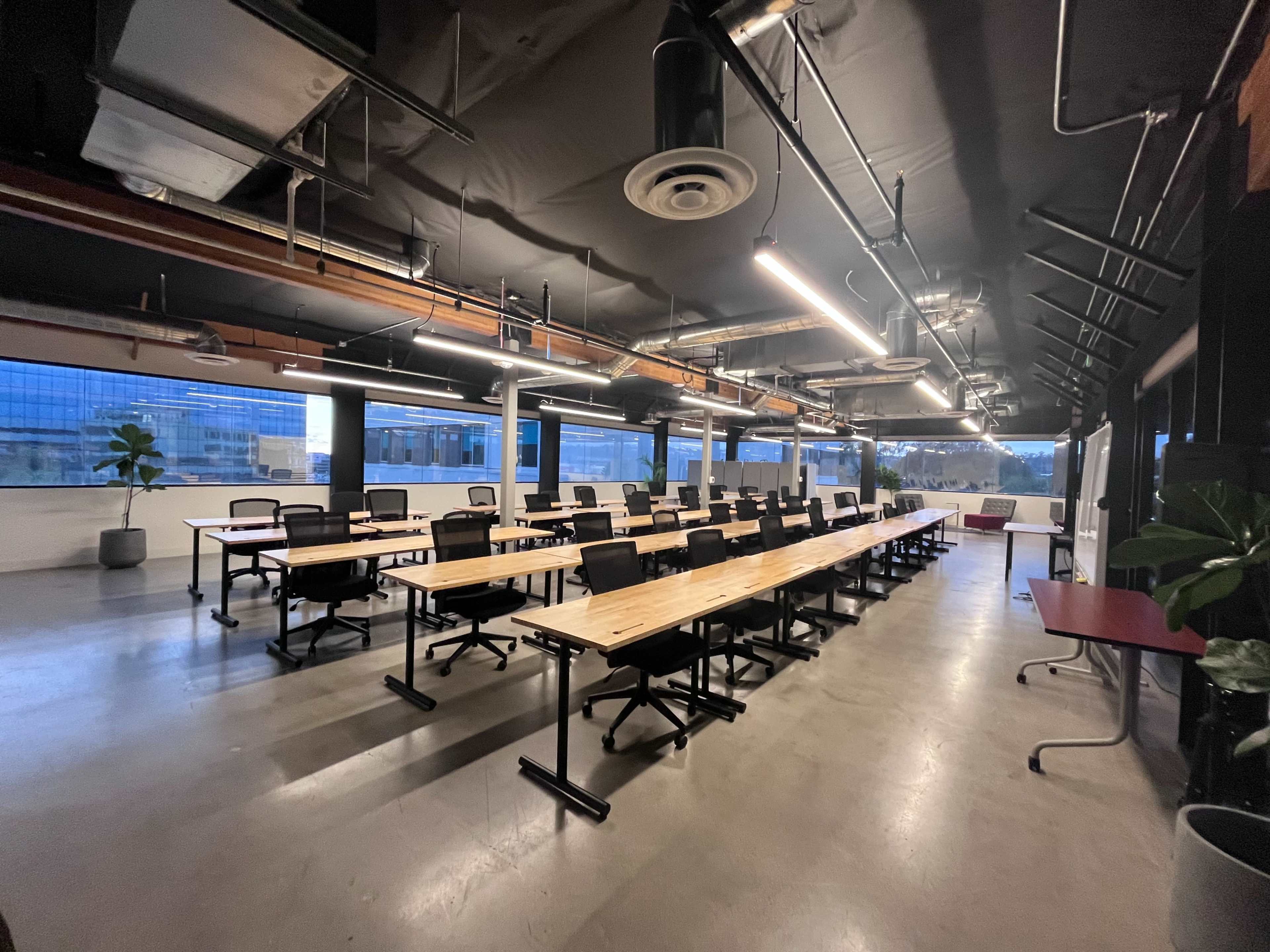 The image shows a spacious, modern conference room with several long tables arranged in a row and large windows showcasing a cityscape.