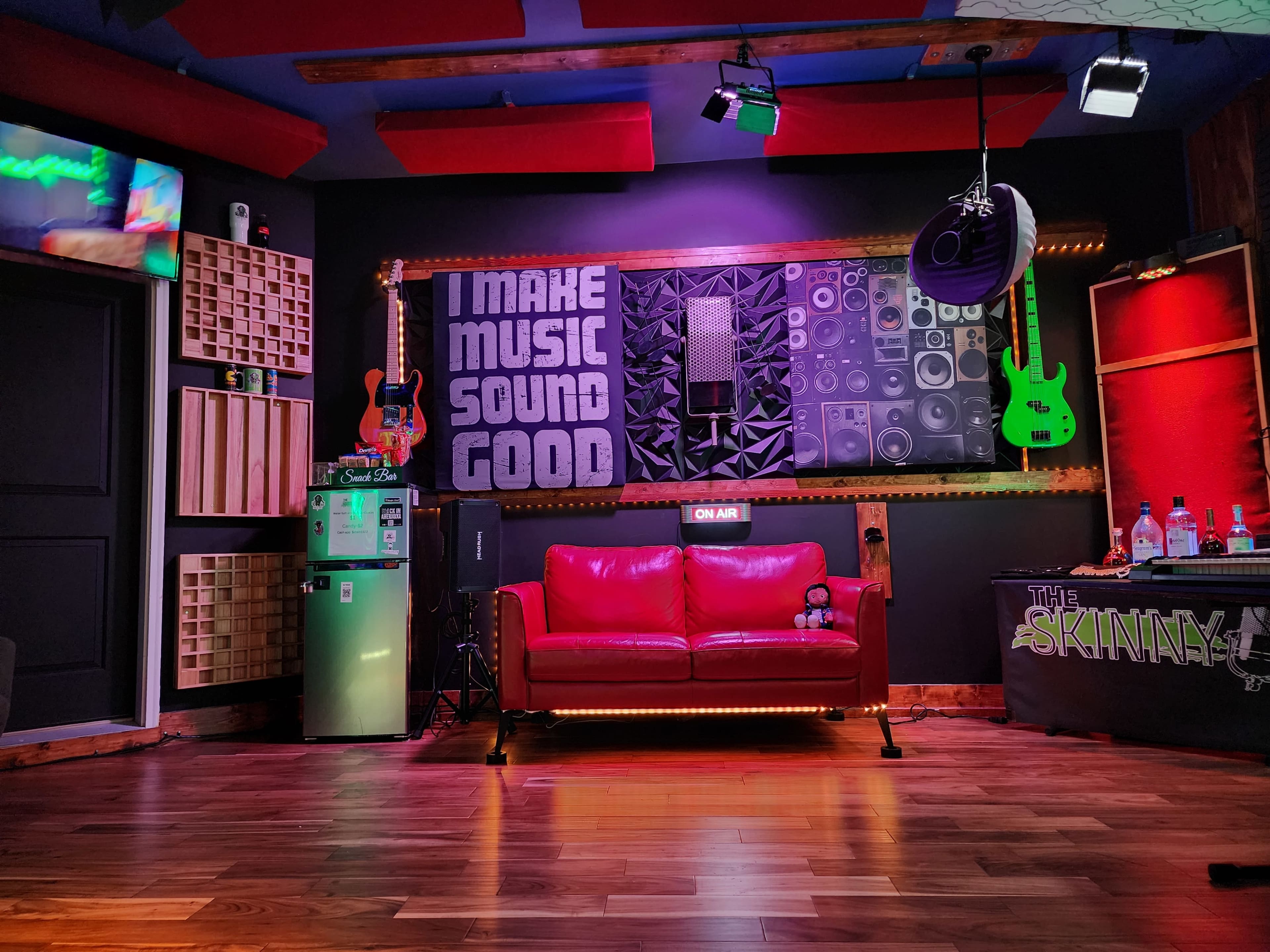 A music-themed studio with a red couch, a wall adorned with speakers and guitars, and colorful lighting.