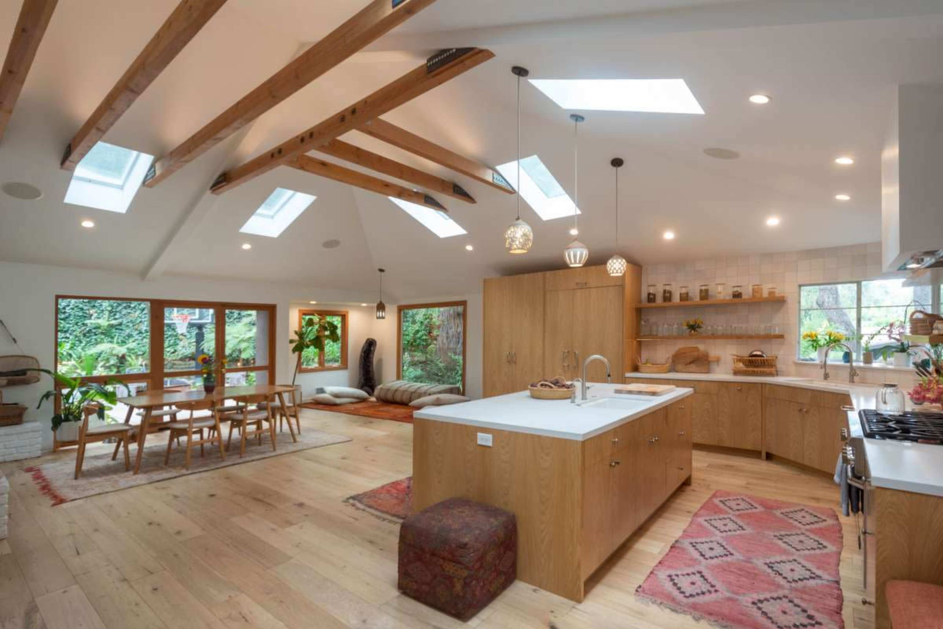 A spacious kitchen features wooden beams, a central island, and large windows that overlook a garden.