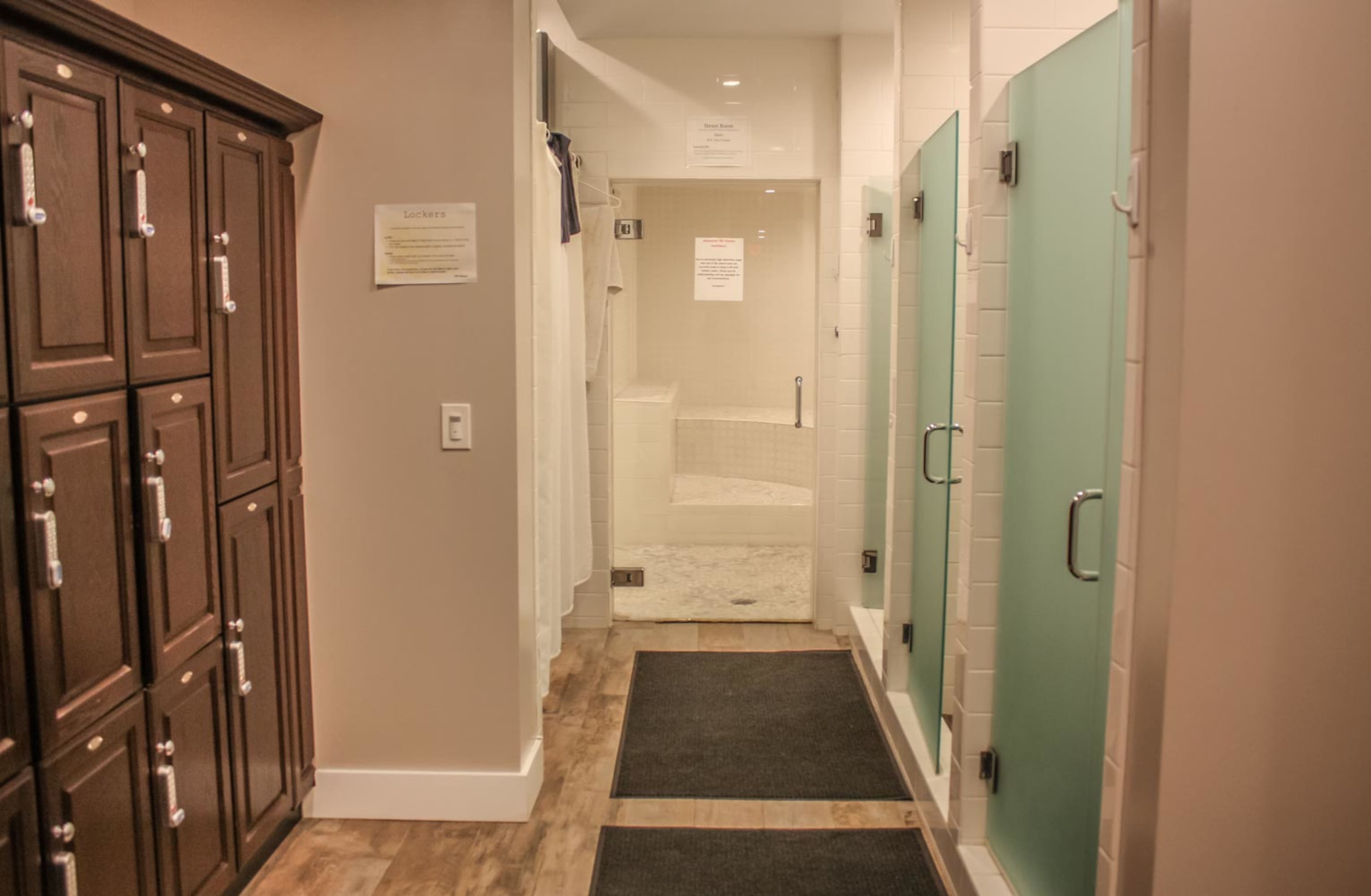 A hallway with wooden lockers on the left and frosted glass shower stalls ahead.
