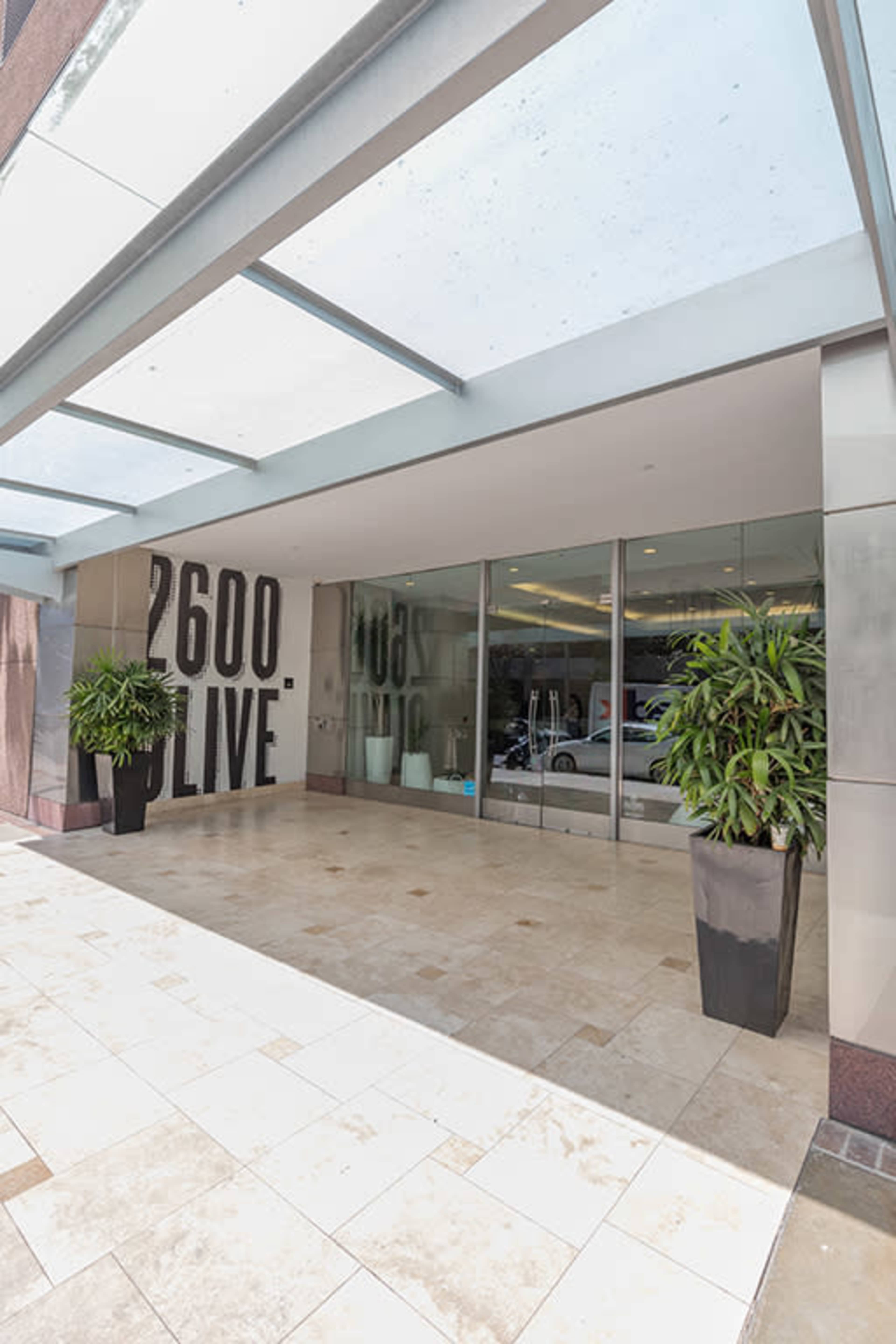 The entrance of a modern building features large glass doors and potted plants, with "2600 LIVE" displayed prominently on the wall.